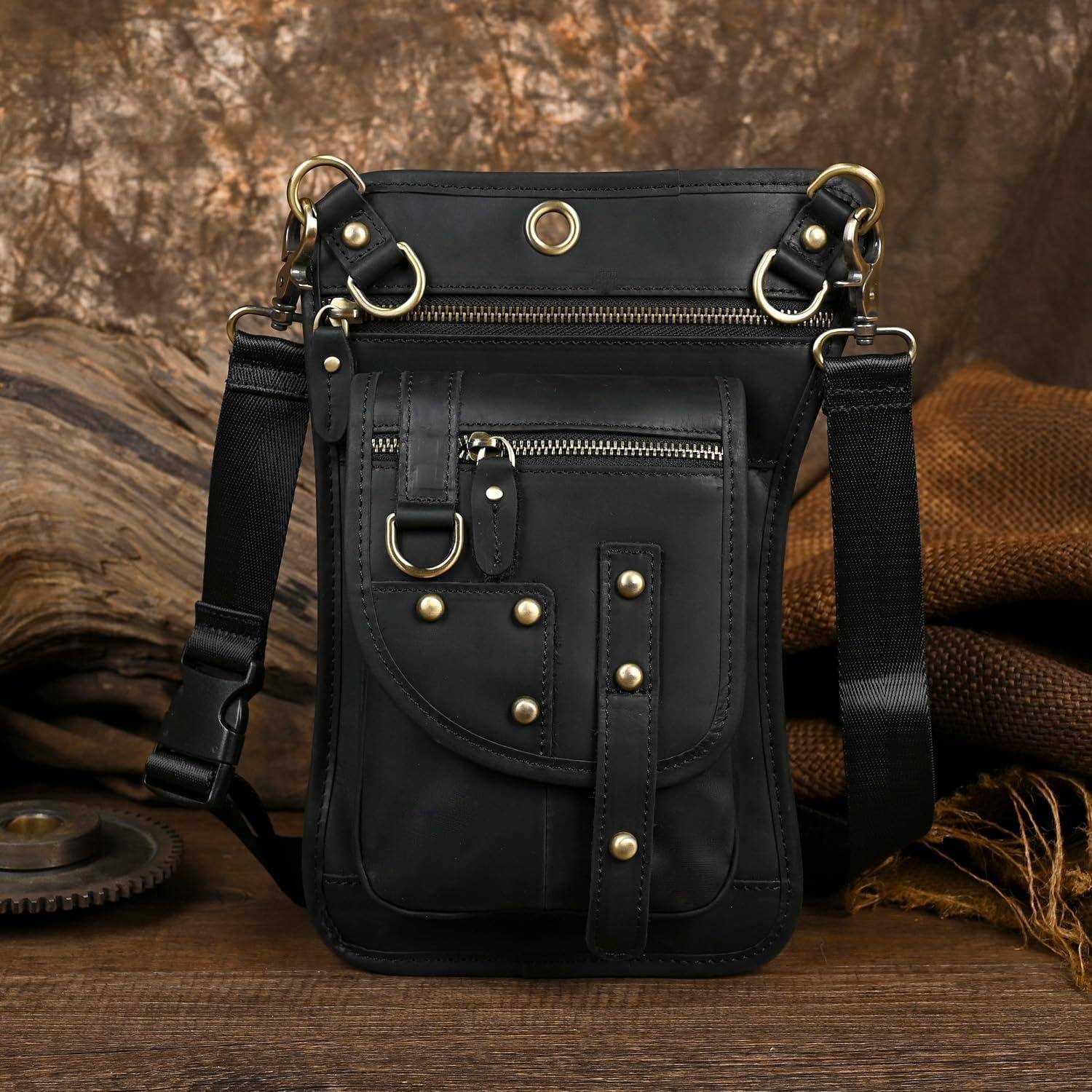 Schwarze Ledertasche mit Schultergurt aus mehreren Reißverschlusstaschen, Metallringen und Nieten auf einer rustikalen Holzoberfläche.