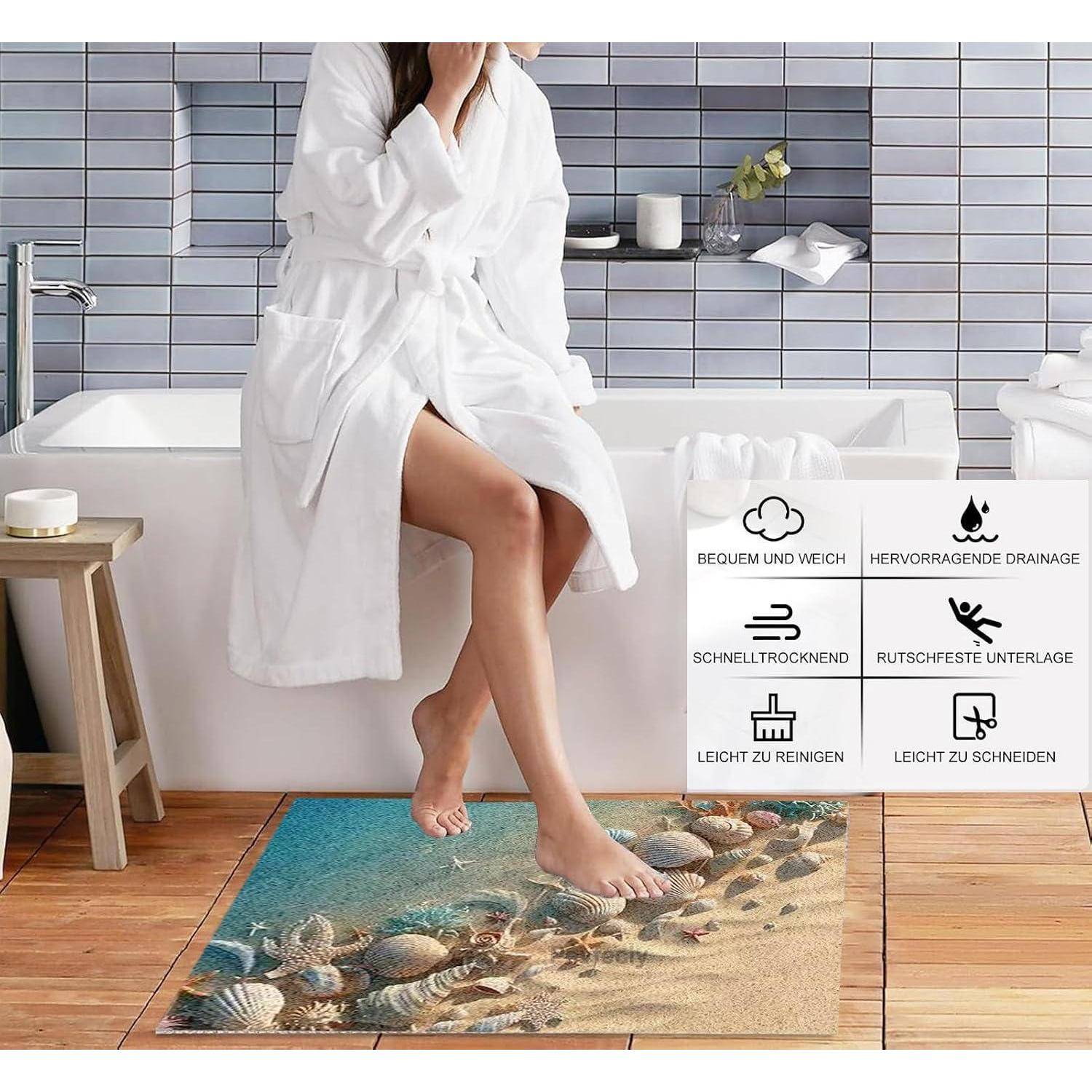 Eine Frau in einem weißen Bademantel sitzt auf dem Rand einer Badewanne und zeigt eine blau-sand-farbene Badematte mit Muschel-Design und Symbolen, die schnelle Trocknung, Rutschfestigkeit und einfache Reinigung bewerben.