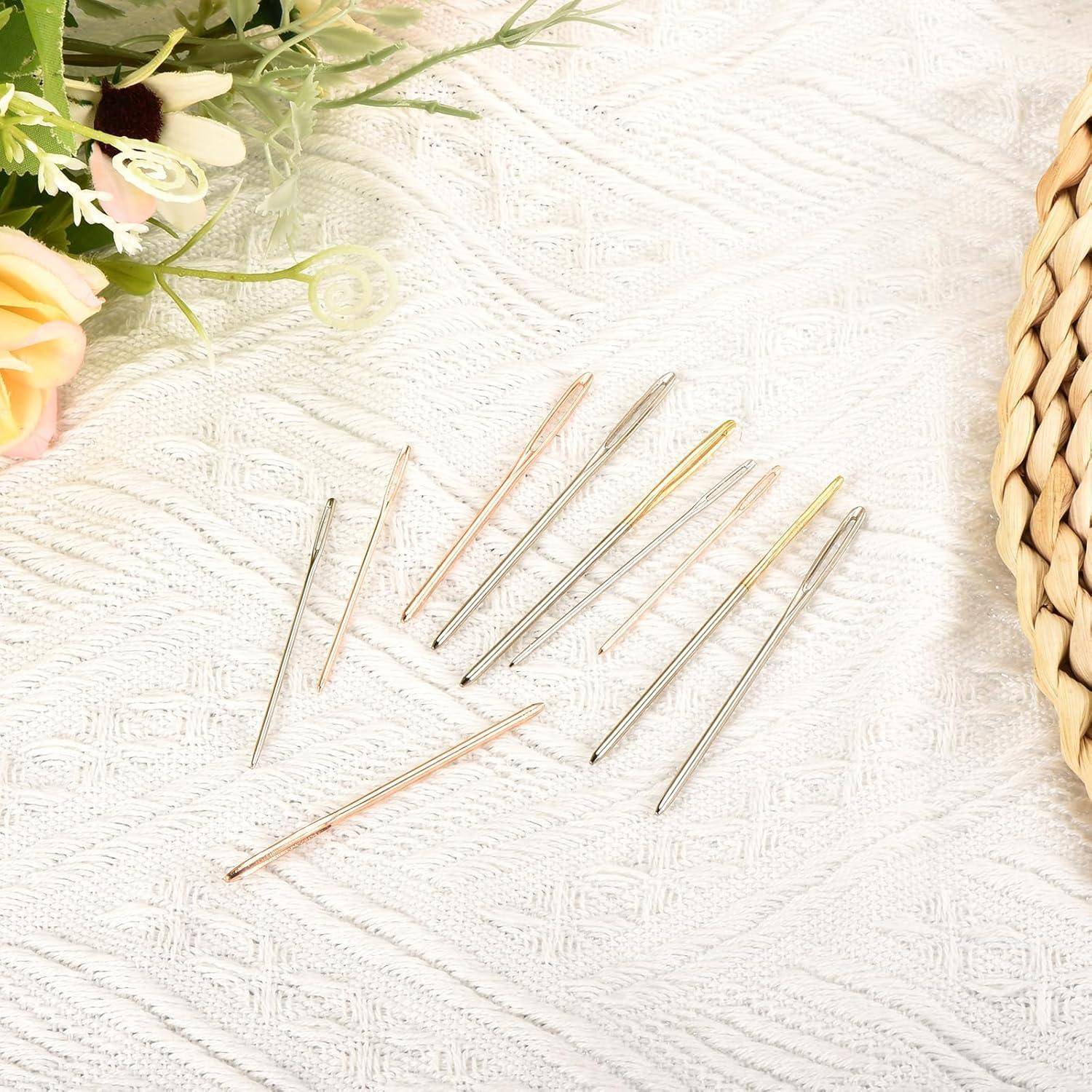 Assortierte Metallnähnadeln, verstreut auf einem weißen strukturierten Stoffhintergrund, mit Blumen oben links und einem geflochtenen Korb auf der rechten Seite.