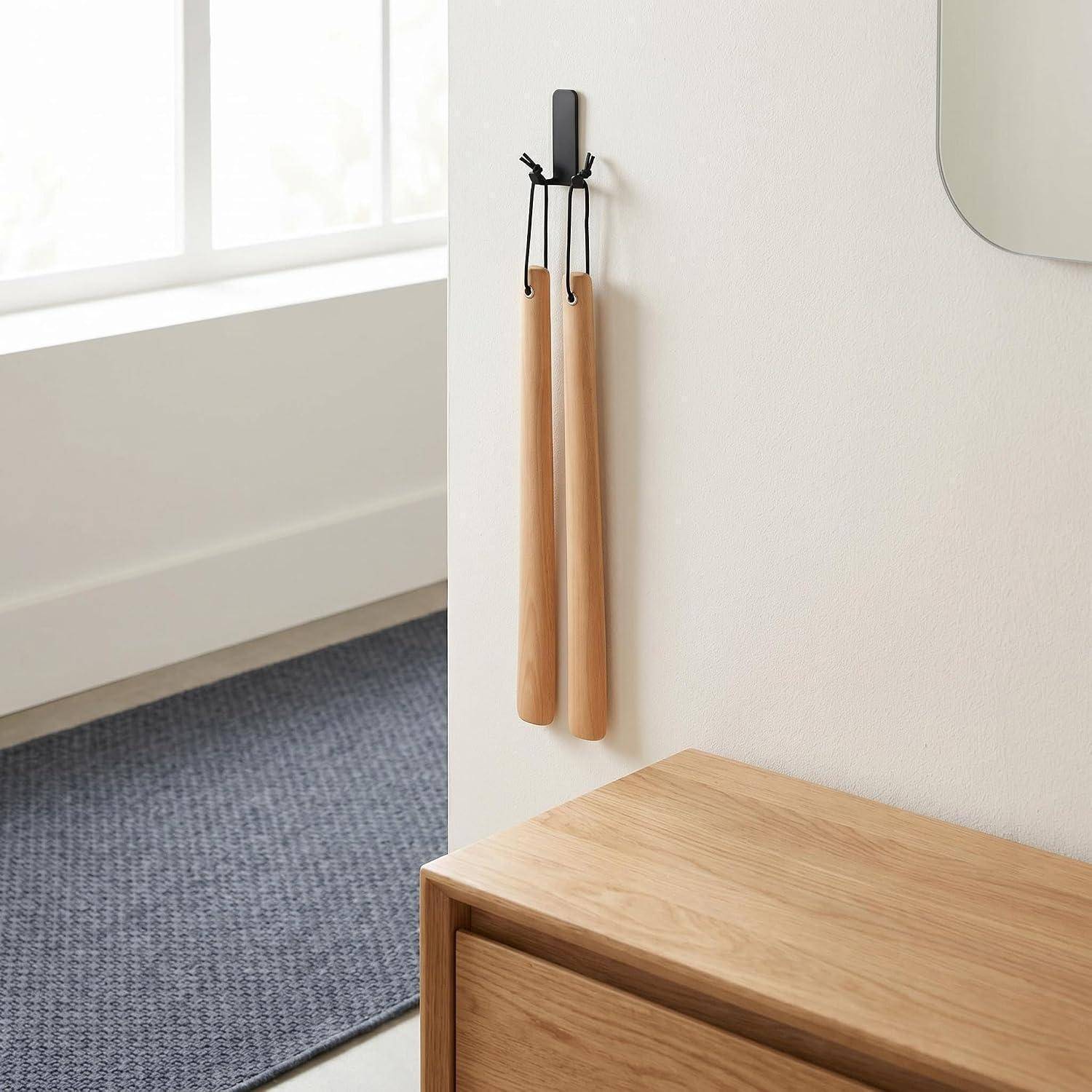 Zwei hölzerne Massagegeräte hängen an einem Wandhaken über einem Holzschrank in einem minimalistischen Zimmer in der Nähe eines Fensters.