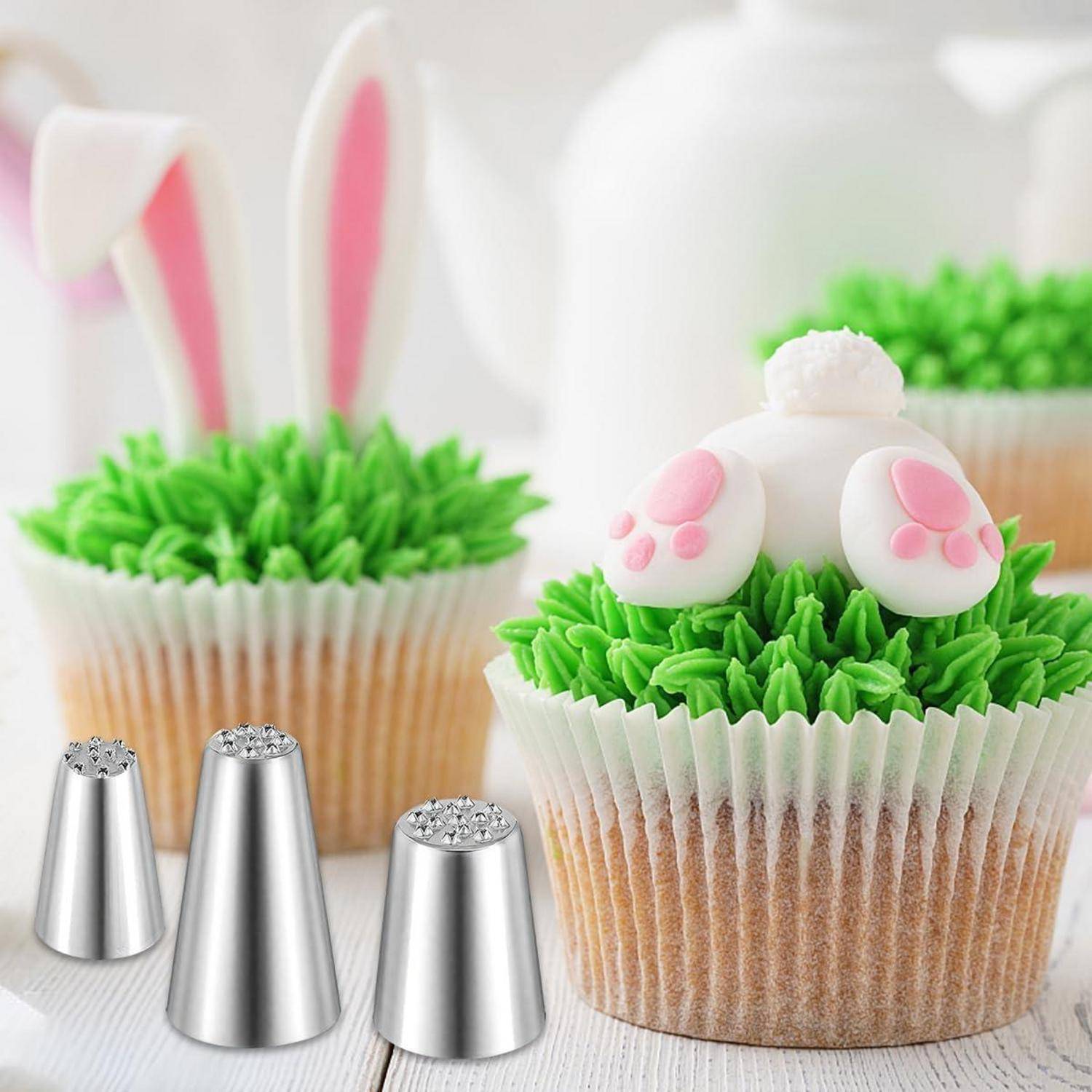 Oster-Cupcakes dekoriert als Hasenhinterteile mit rosafarbenen Pfoten und grünem Zuckerguss-Gras, mit Metall-Spritztüllen im Vordergrund.