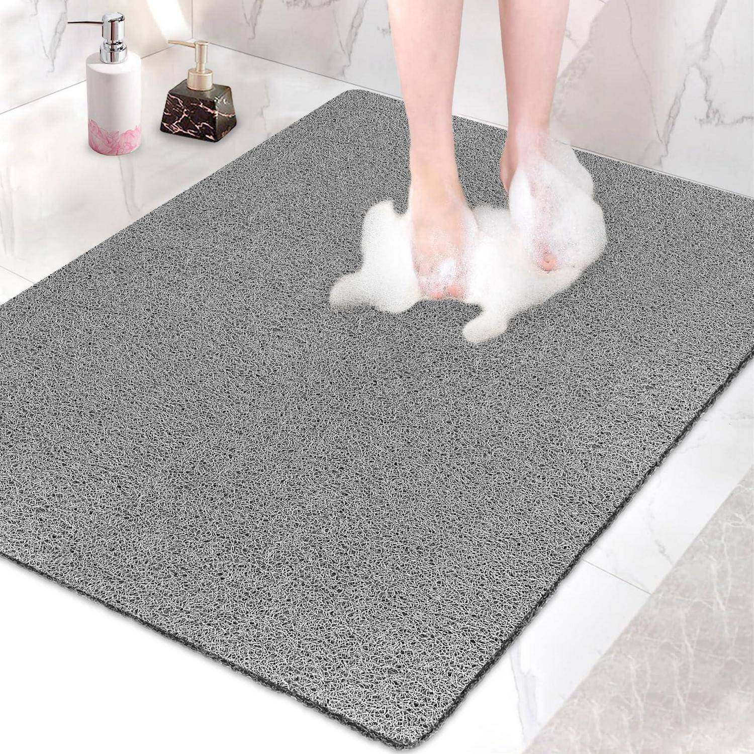 Füße, die auf einer grauen strukturierten Badewannenmatte im Badezimmer gerieben werden, zeigen eine rutschfeste Bodenmatte mit Seifenschaum.