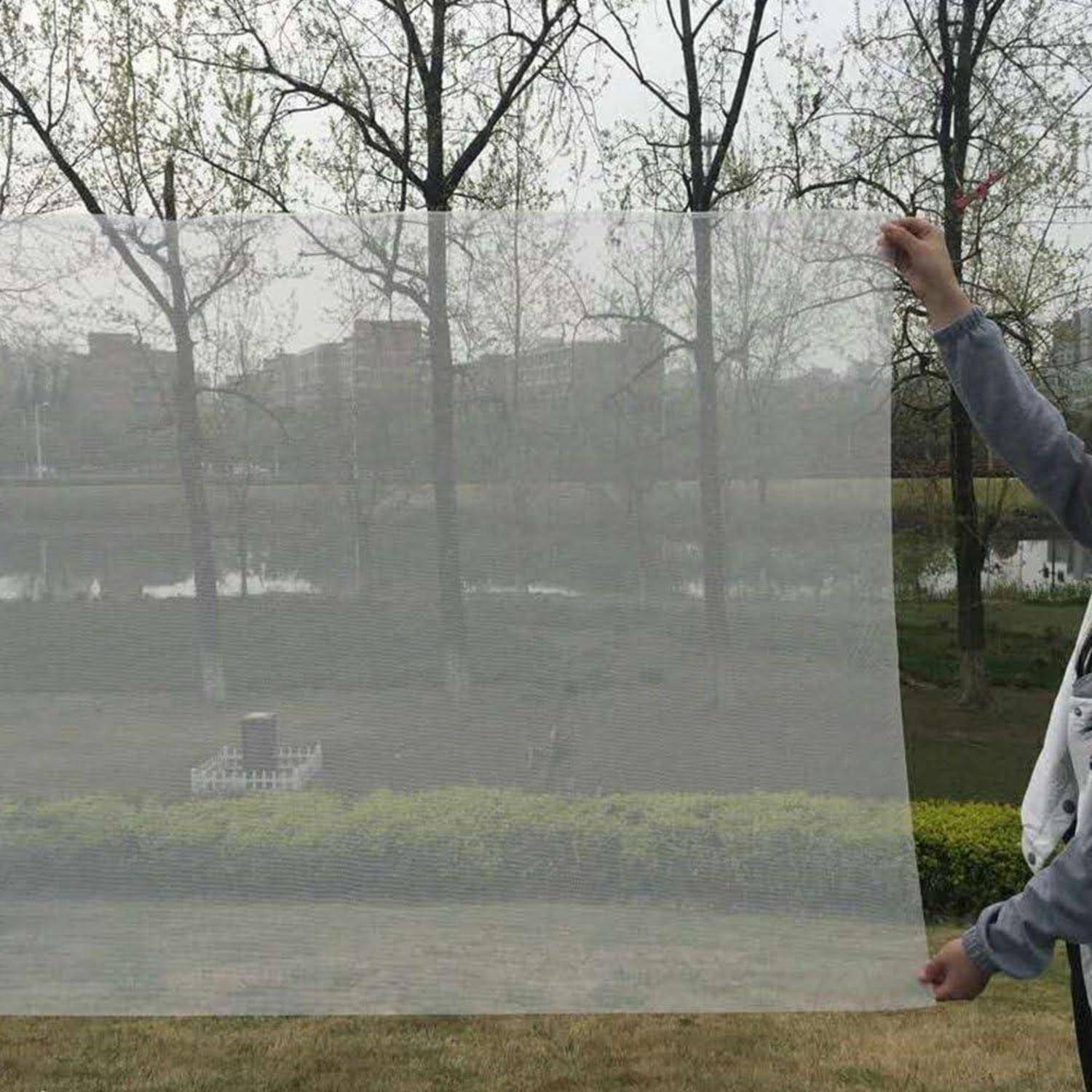 Eine Person hält einen großen durchscheinenden Maschenbildschirm im Freien hoch und zeigt, wie dieser die Sichtbarkeit filtert, während er Bäume und Landschaft dahinter noch offenbart.