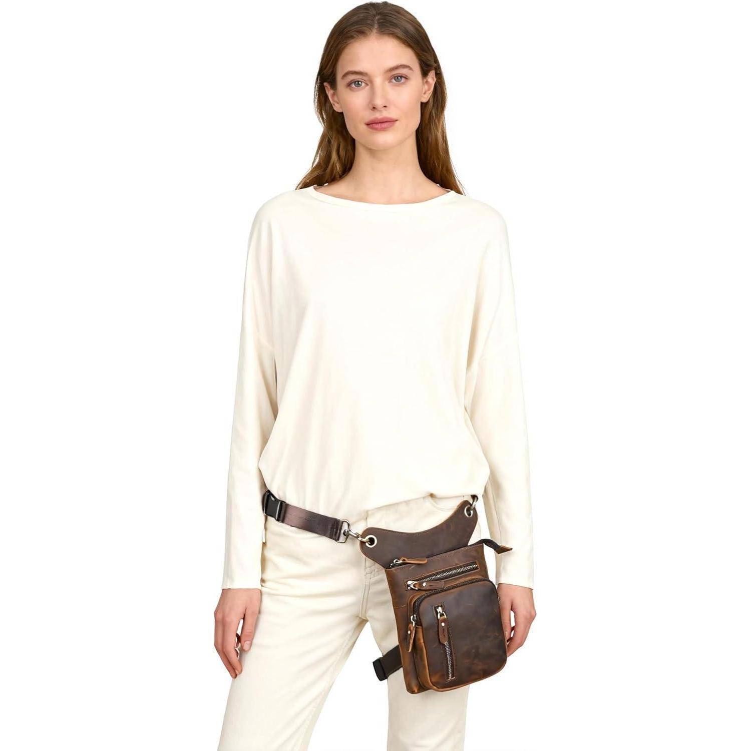 Frau in cremefarbenem Outfit mit einer braunen Crossbody-Utilitytasche, die auf der Hüfte getragen wird, vor einem einfachen weißen Hintergrund.