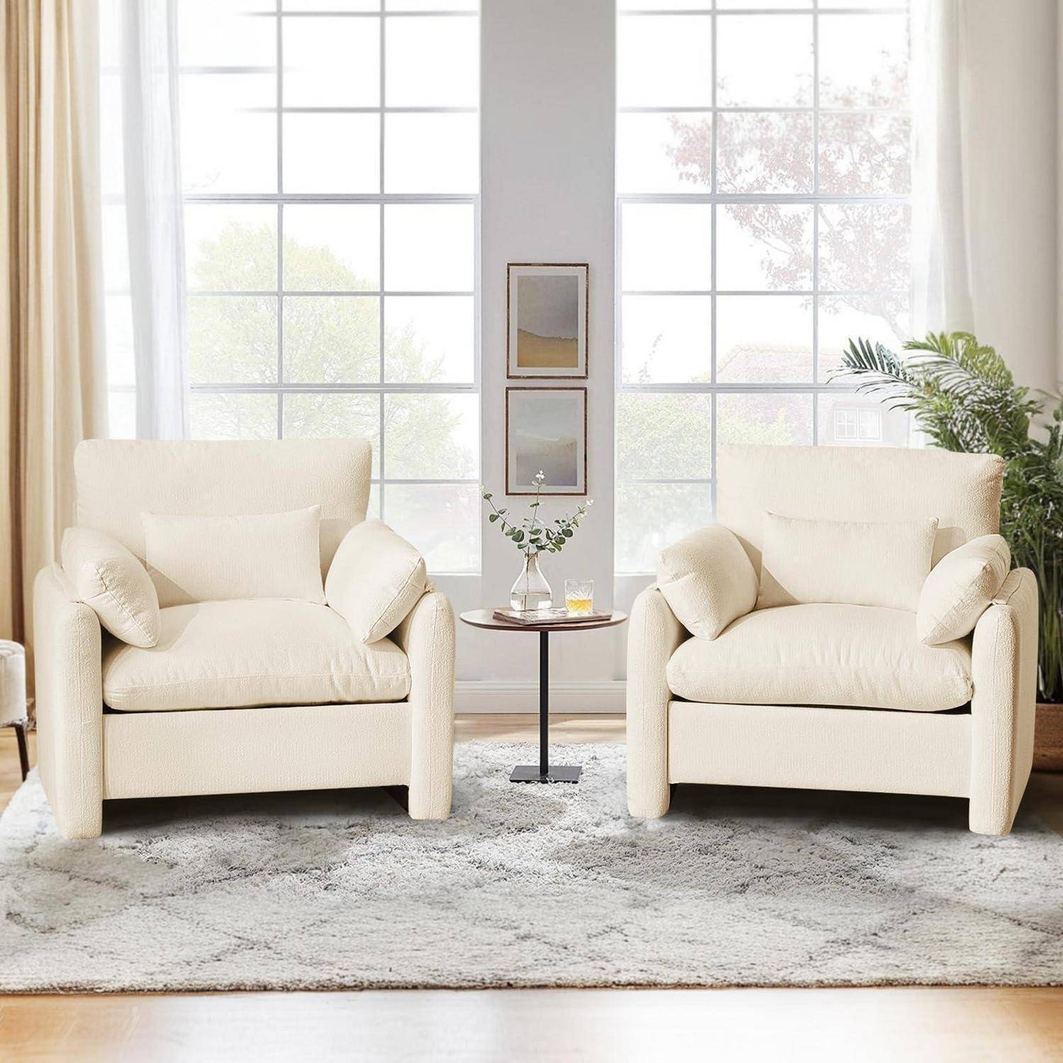 Helles Wohnzimmer mit zwei cremefarbenen Sesseln, die sich ein kleines rundes Tischchen zwischen großen Fenstern gegenüberstehen, stilvoller dekoriert mit einer Pflanze und gerahmten Wandbildern.