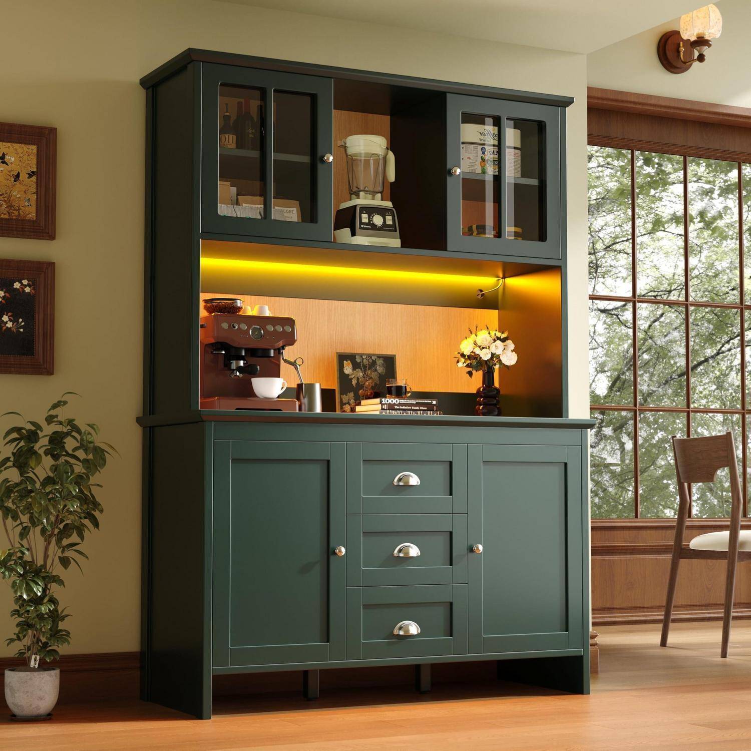 Dunkler grüner Glasschrank mit Glastüren, Regalen und eingebauter Beleuchtung, der neben einem Fenster einen Mixer, eine Espressomaschine, Tassen, Bücher und Blumen enthält.