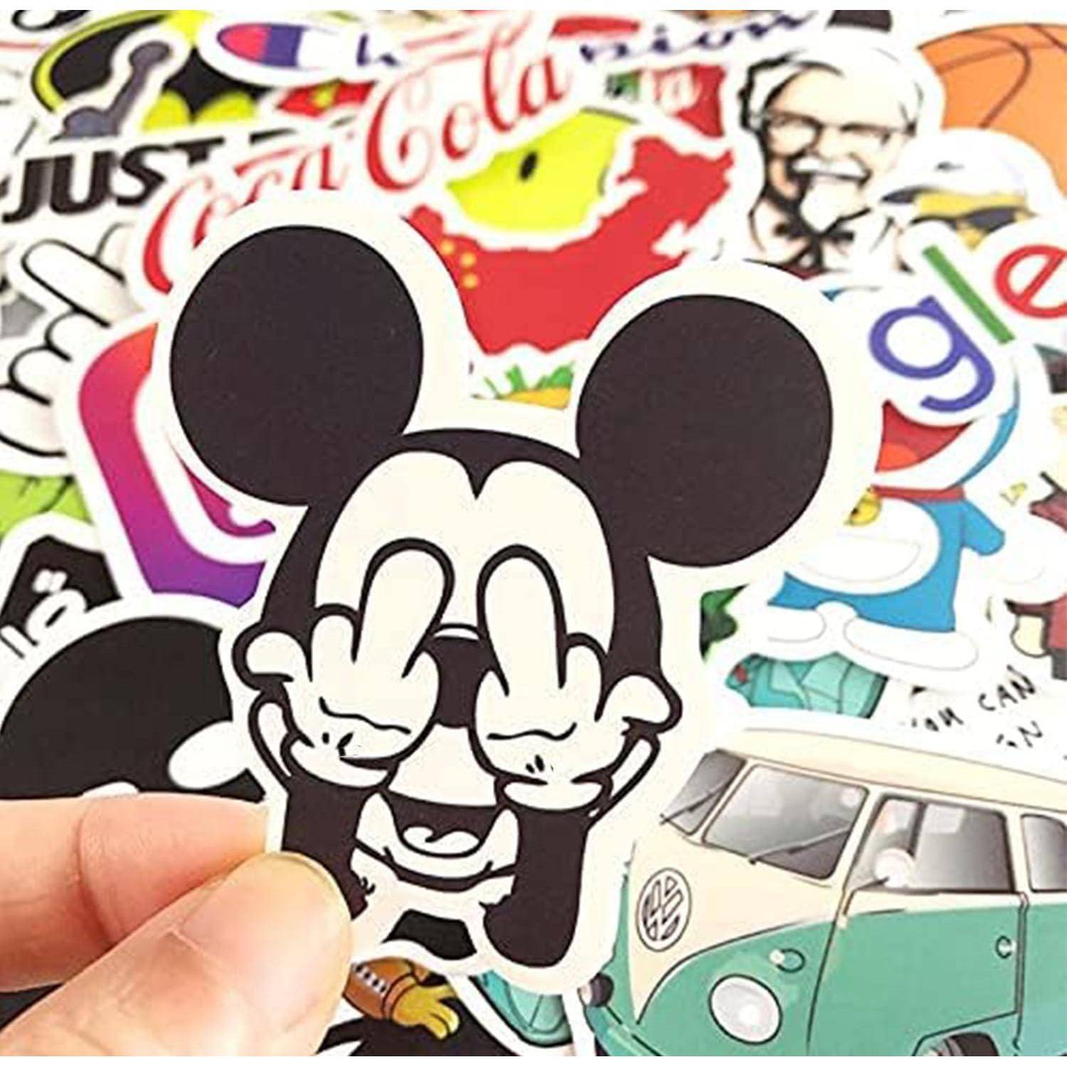 Hand hält einen schwarz-weißen Cartoon-Mickey-Mouse-Aufkleber über einen verstreuten Stapel von farbenfrohen Reise- und Markenaufklebern.