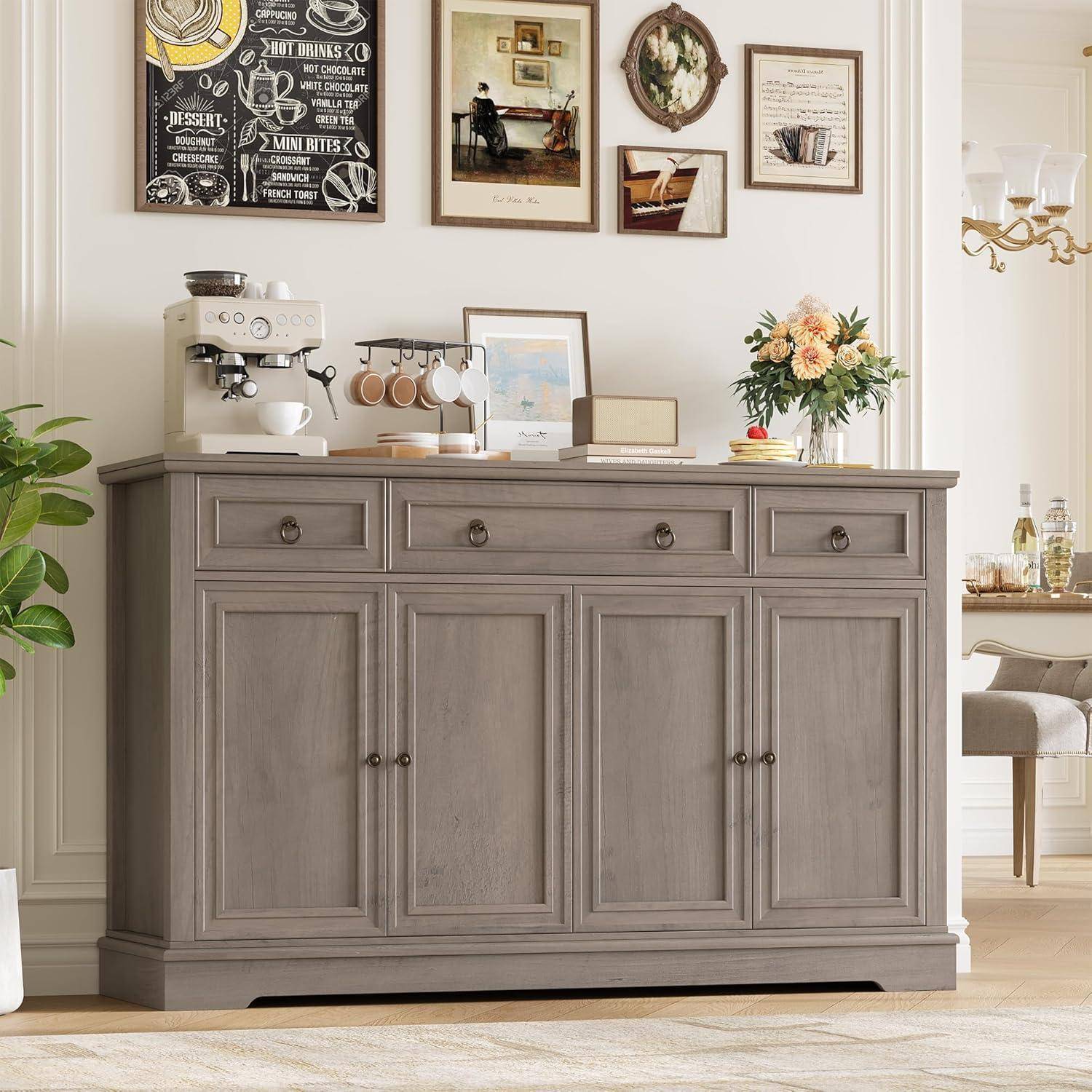 Graue Holzkommode in einem Esszimmer, darauf eine Kaffeemaschine, Tassen, gerahmte Kunstwerke und Blumen.