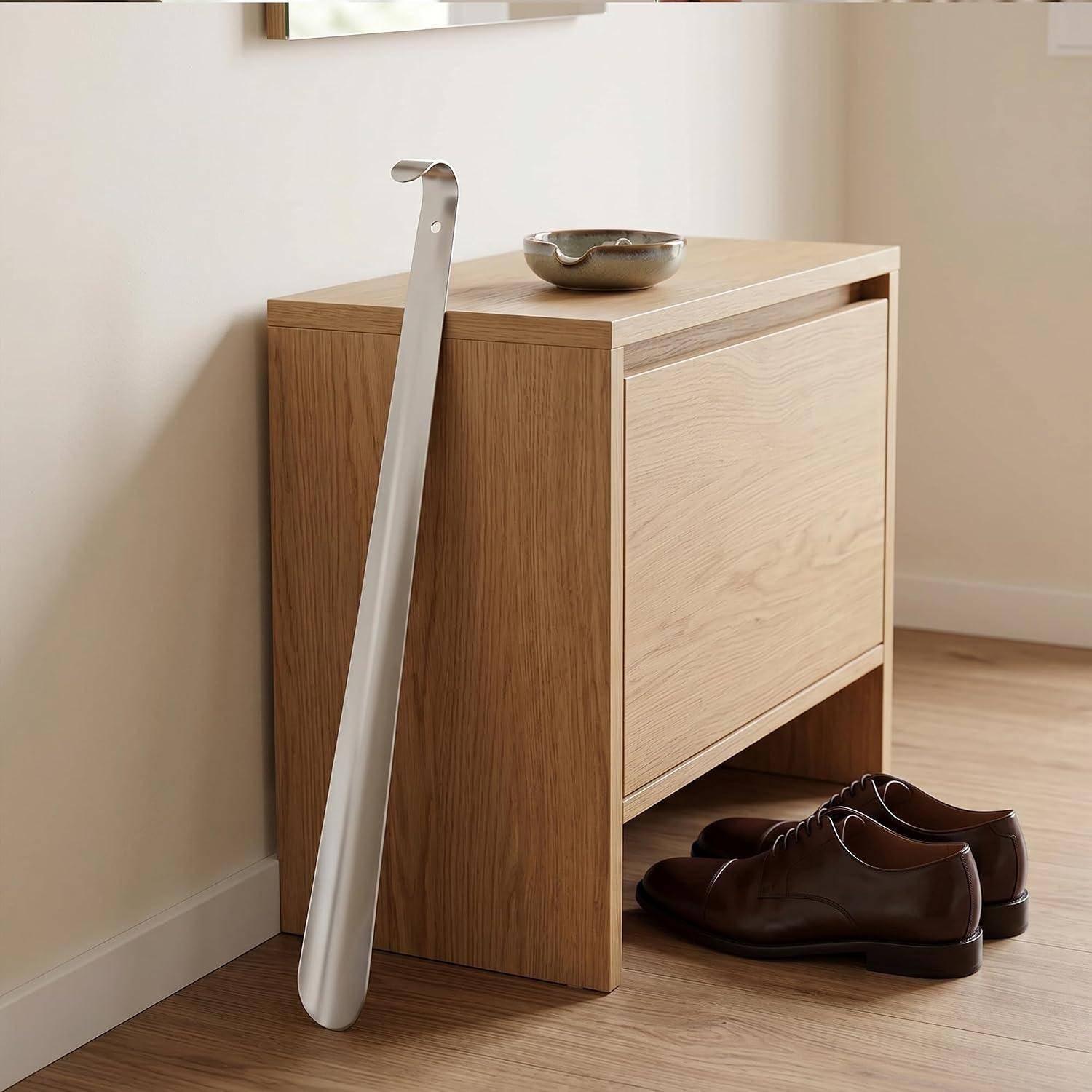 Holzschrank für Schuhe mit einem Schuhlöffel, der daran lehnt, und Anzugschuhe, die darunter in einem minimalistischen Zimmer gelagert sind.