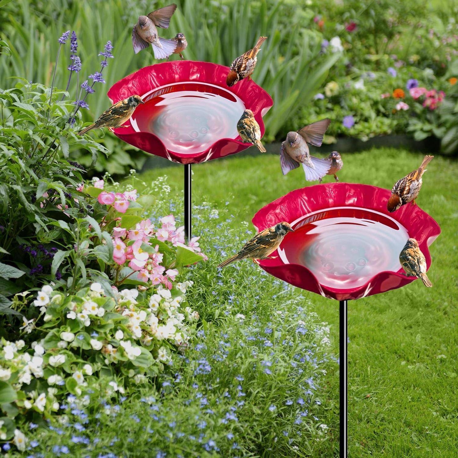 Zwei rote blumenförmige Vogelfutterstellen in einem Garten, mit mehreren Kolibris, die unter grünen Pflanzen und Blumen fressen.