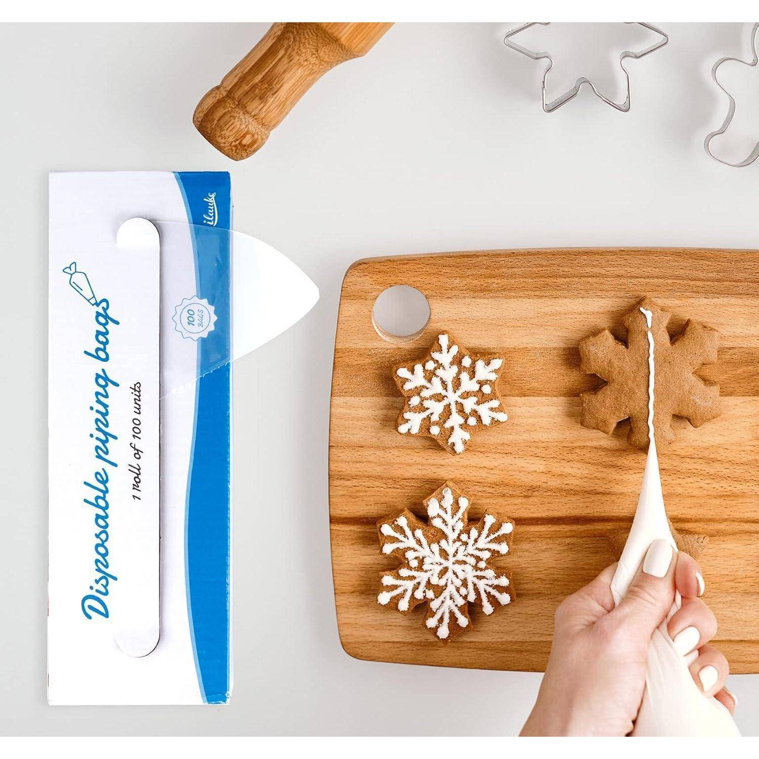 Hand legt ein Schneeflocken-Keks mit einer weißen Spritzbeutel auf ein Holzbrett neben einer Schachtel mit der Aufschrift „Einweg-Spritzbeutel