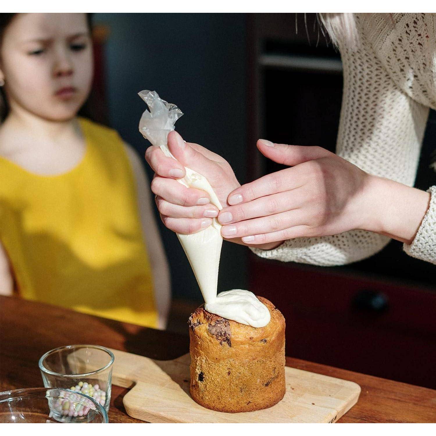 Eine Person spritzt weiße Glasur auf einen kleinen Kuchen auf einem Schneidebrett, während ein Kind in der Nähe zuschaut.
