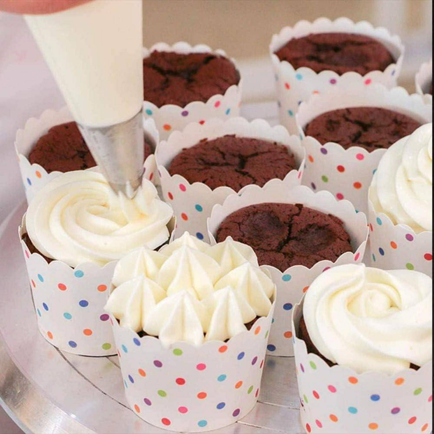 Eine Spritztüte trägt weiße Glasur auf Schokoladen-Cupcakes in Papierkapseln mit Polka-Dot-Muster auf einem Tablett auf.