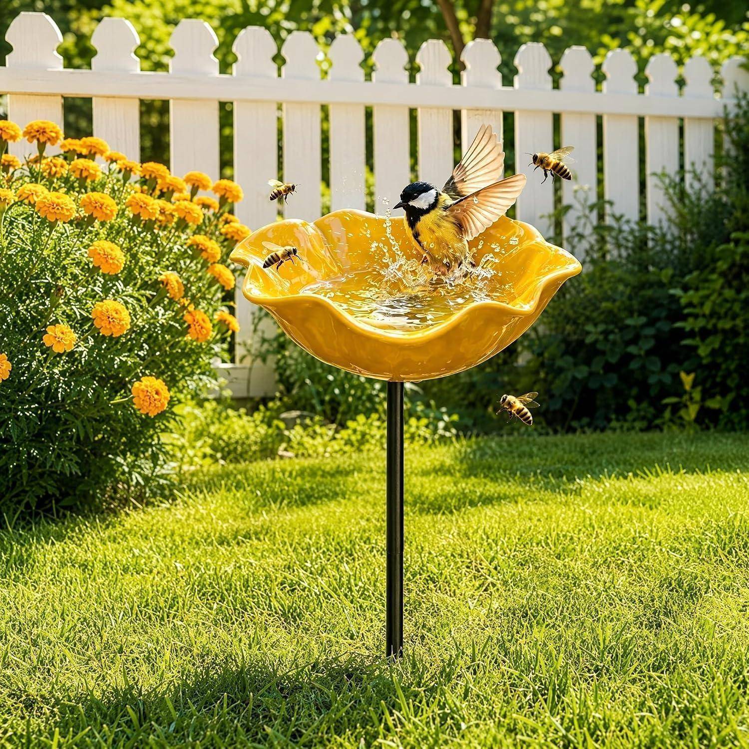 Vogeltränke in einem sonnigen Garten mit einem kleinen Vogel, der im Wasser planscht, umgeben von mehreren Bienen in der Nähe von orangefarbenen Blumen und einem weißen Lattenzaun.
