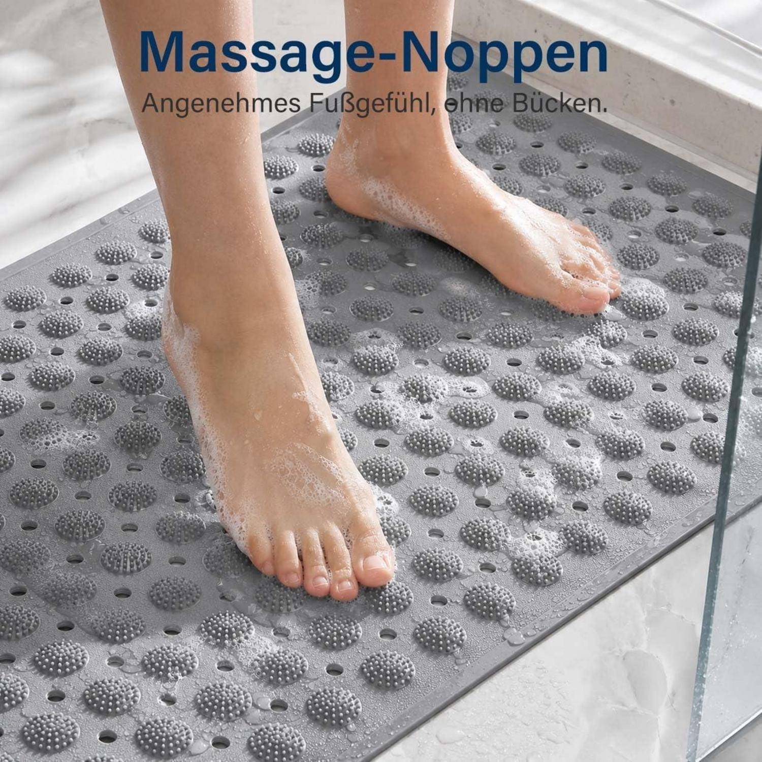 Nahaufnahme von nackten Füßen, die auf einer grauen Massage-Badematte mit erhabenen Punkten stehen; der Text lautet „Massage-Noppen