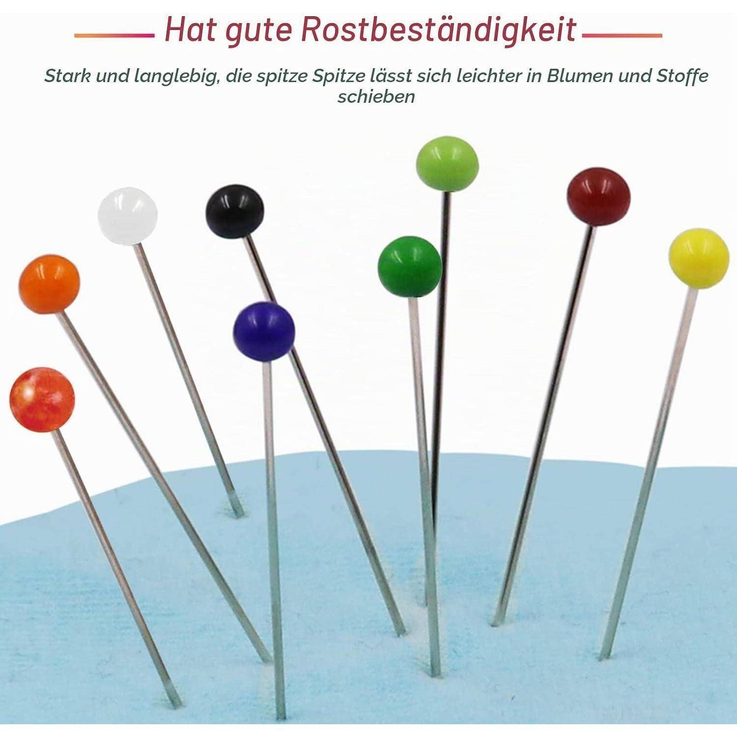 Farbenfrohe gerade Stecknadelköpfe in einem blauen Kissen, die rostbeständige Nadeln mit spitzen Enden demonstrieren, die leicht in Blumen und Stoff gleiten.