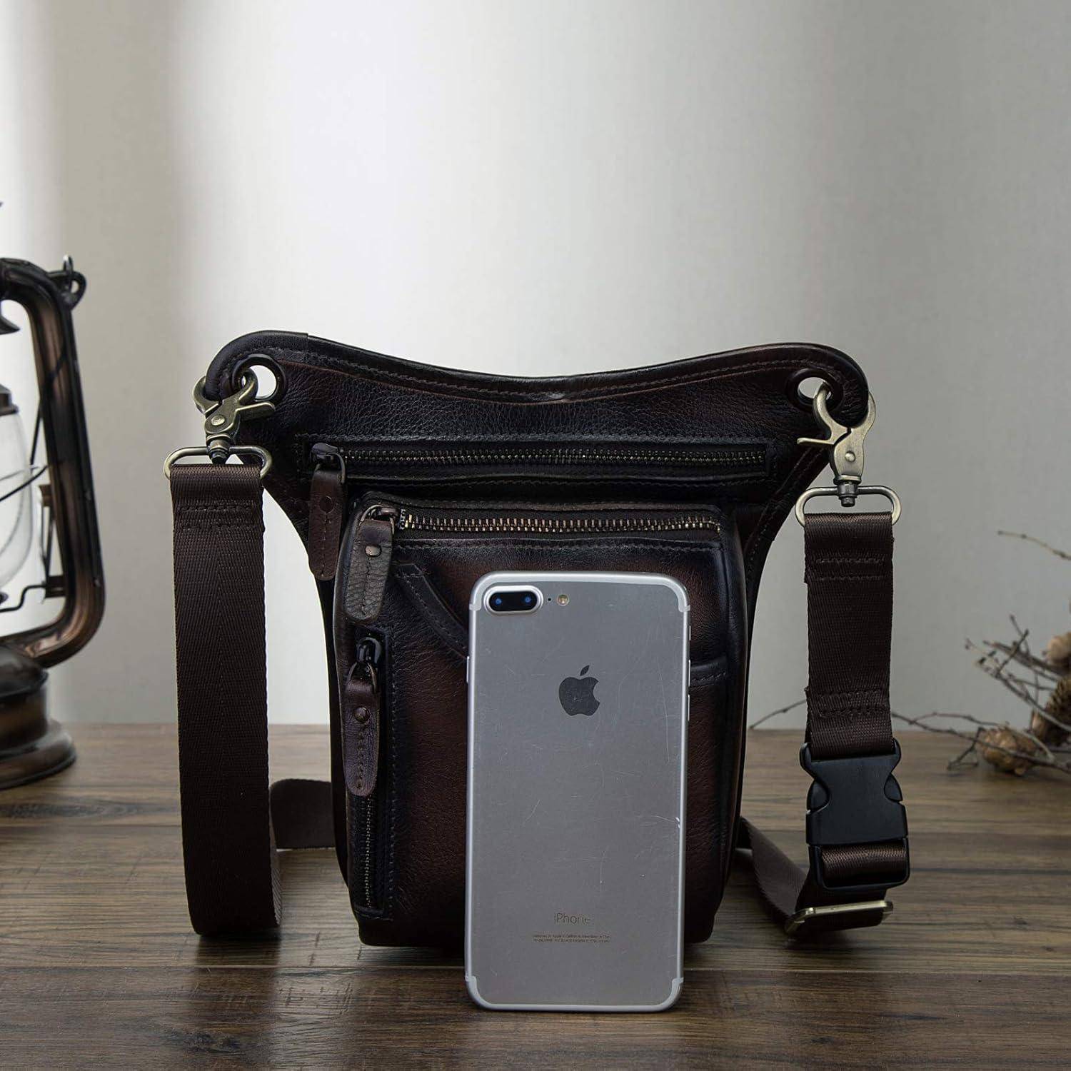 Eine dunkle Ledertasche mit Schultergurt auf einem Tisch, mit einem silbernen iPhone, das an der vorderen Tasche angelehnt ist, zeigt die Größe und die Fächer der Tasche.