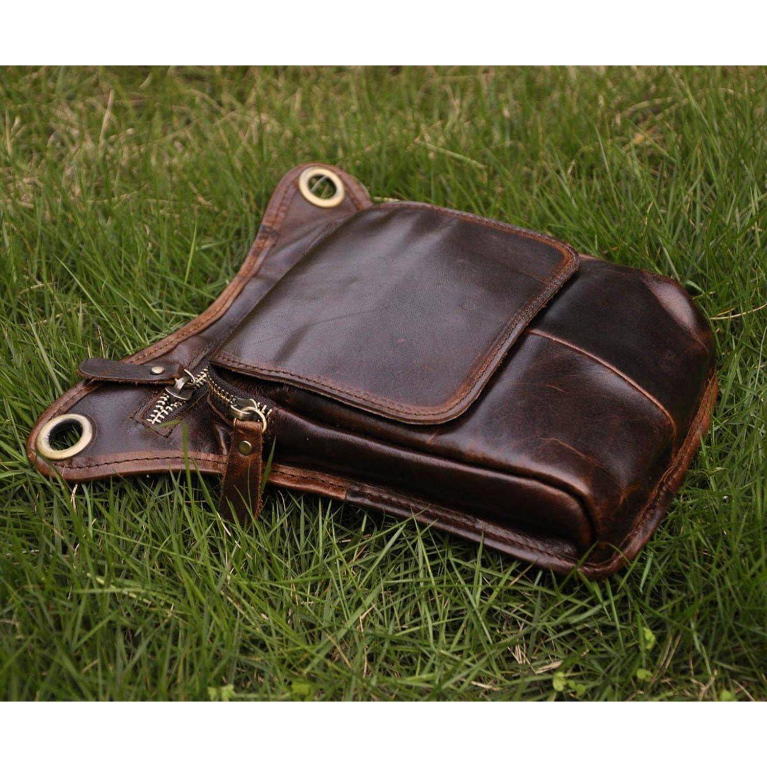 Braune Lederschultertasche mit Vorderlasche und Metallösen, die auf Gras im Freien liegt.