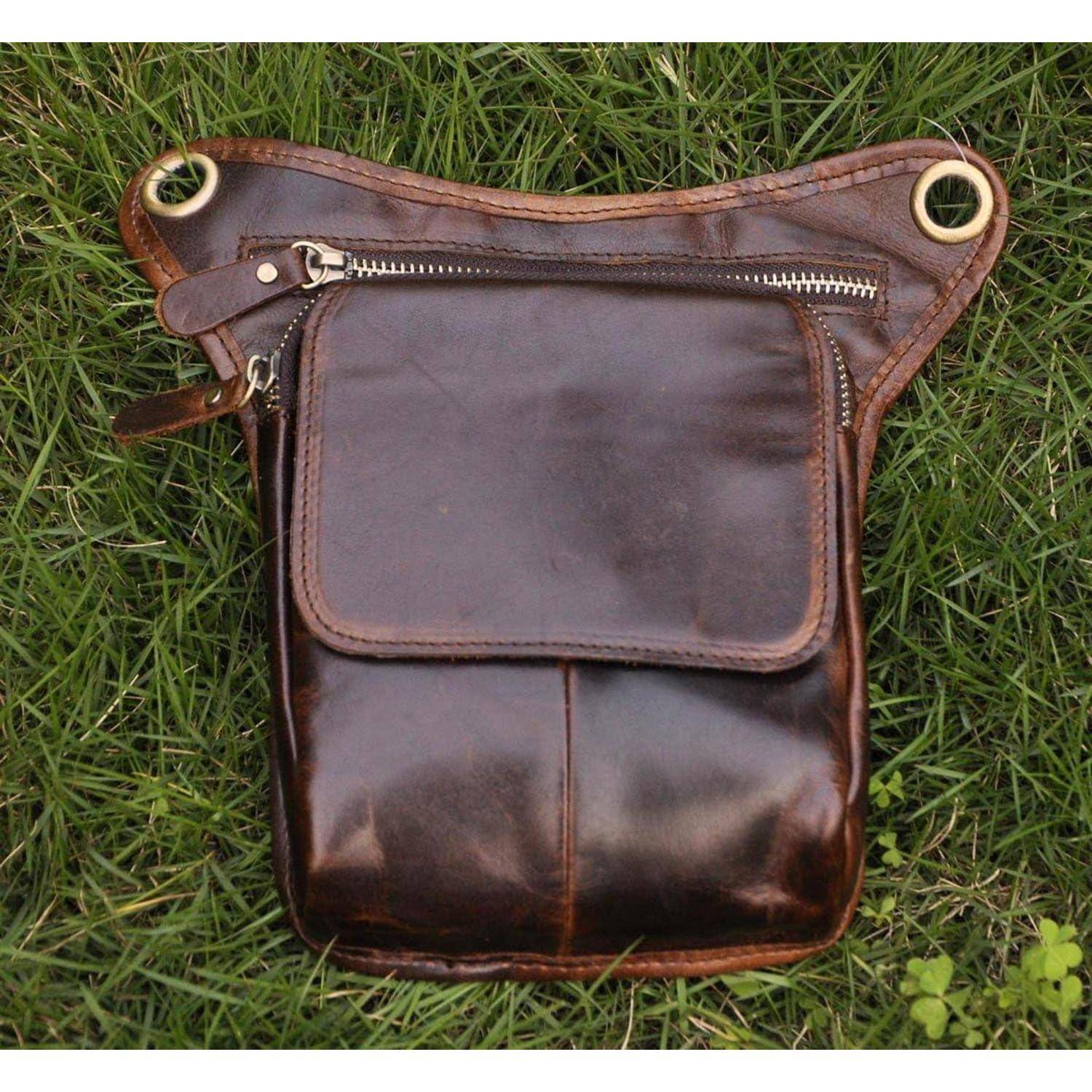 Braune Ledertasche oder kleine Tasche mit vorderer Klappe und Reißverschluss, liegend auf Gras.
