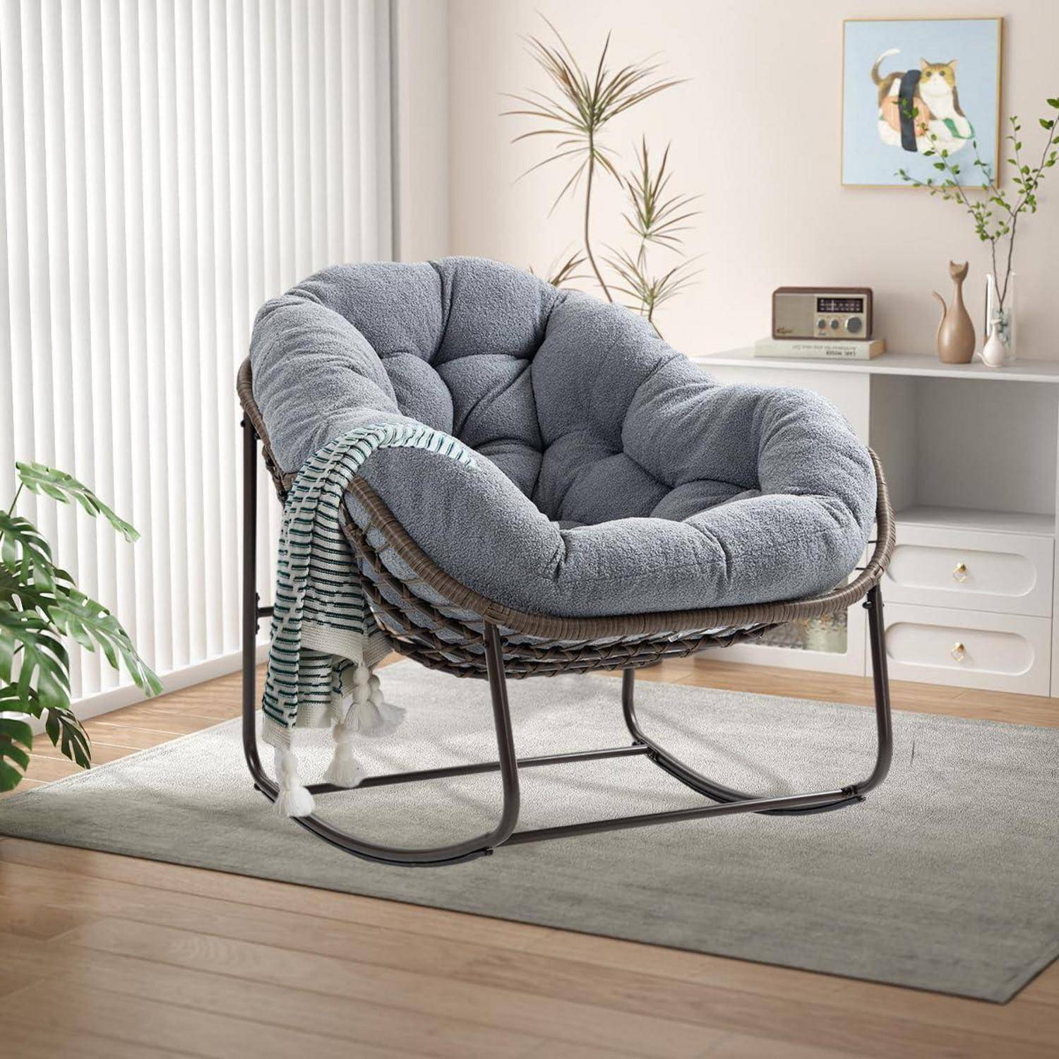 Grauer, gepolsterter Papasan-Stuhl mit dunklem Metallrahmen und gestreifter Wurfdecke in einem hellen Wohnzimmer.