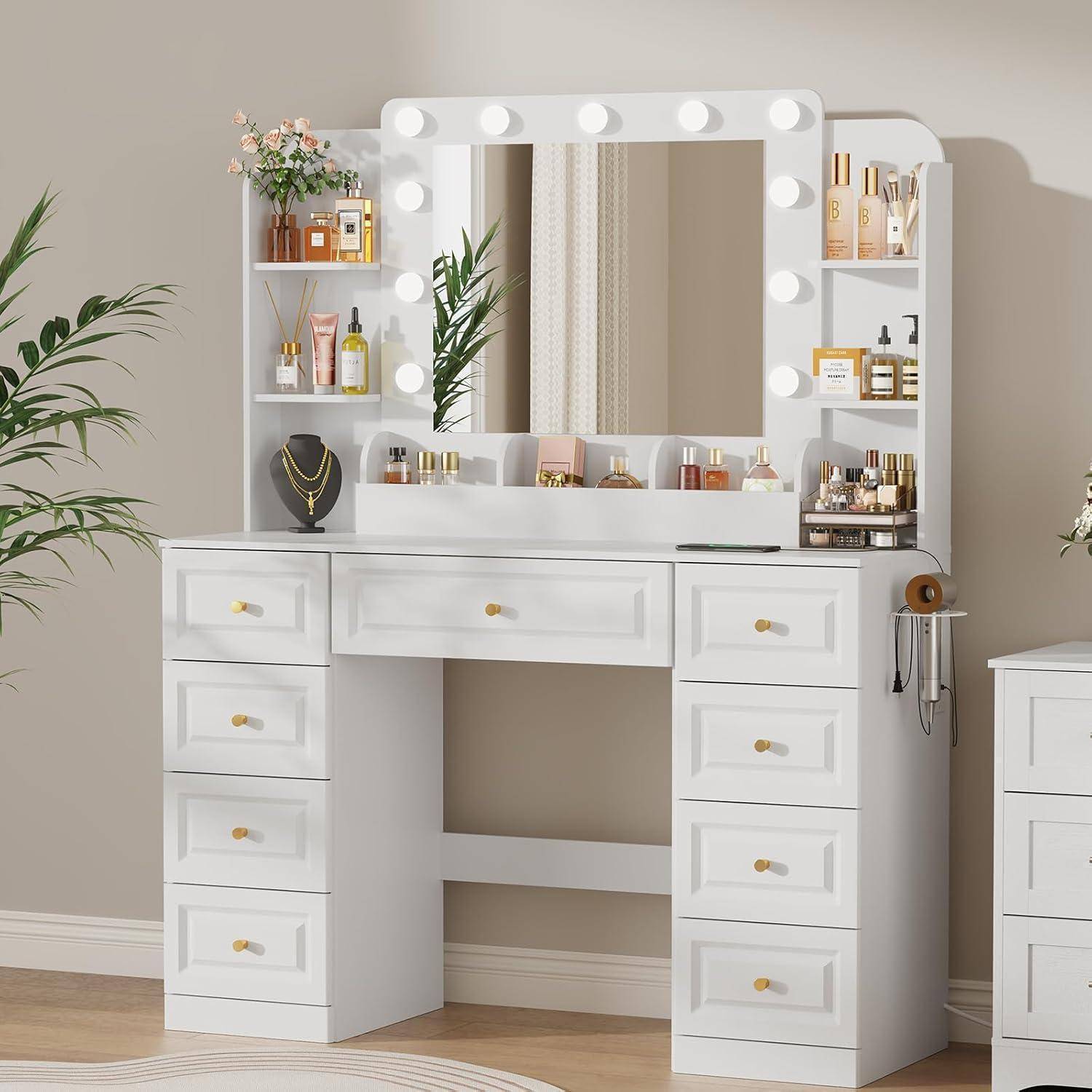 Weißer Schminkschrank mit Spiegelbeleuchung, Regale mit Kosmetik und Parfüm sowie goldener Beschlagware in einem Schlafzimmer oder Ankleideraum.