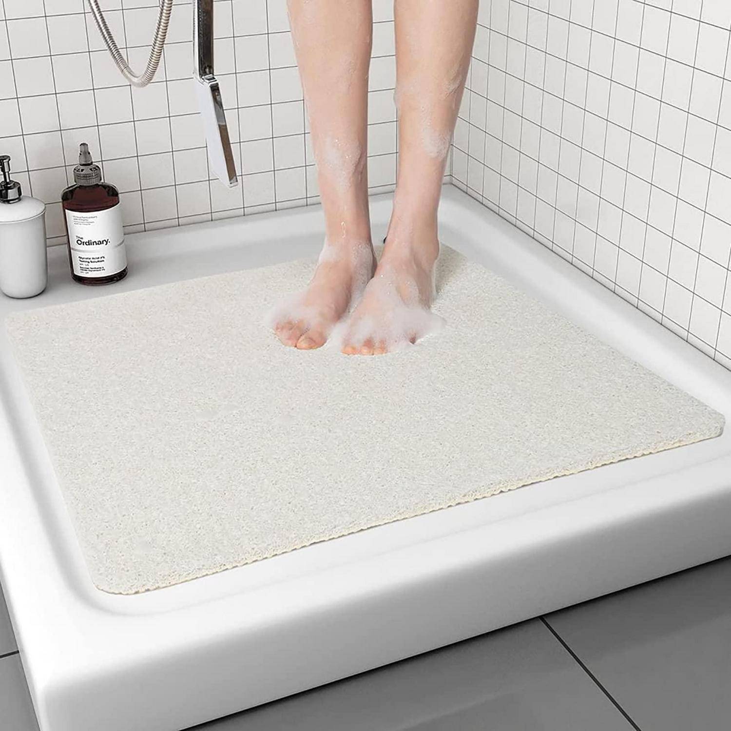 Person, die auf einer großen weißen rutschfesten Matte unter der Dusche steht und ein Badezimmersicherheitszubehör zeigt.