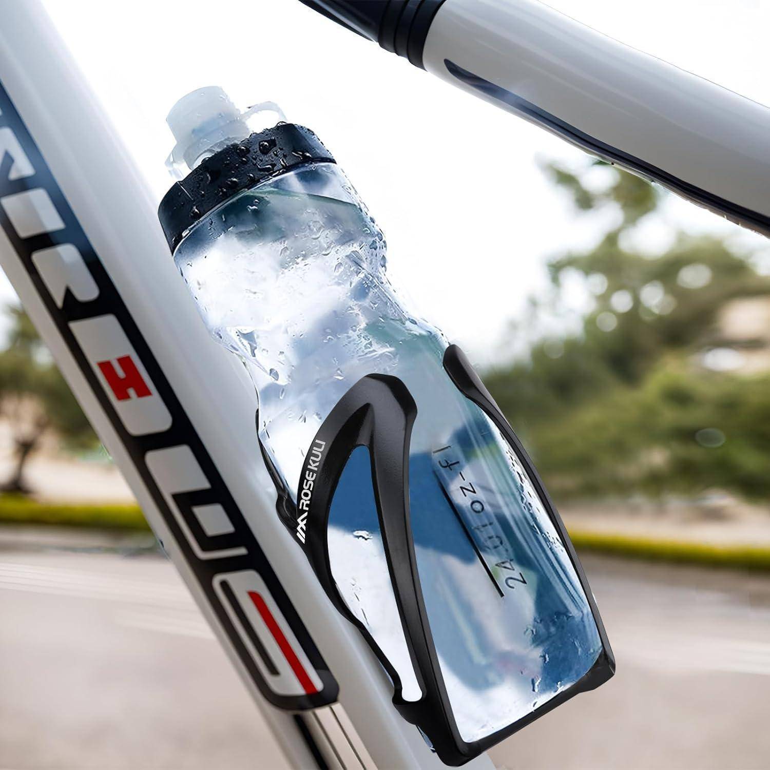 Wasserflasche, die in einem schwarzen Halter auf einem Fahrradrahmen montiert ist, mit Kondensation und sichtbarem Markentext, vor einem unscharfen Außenhintergrund.