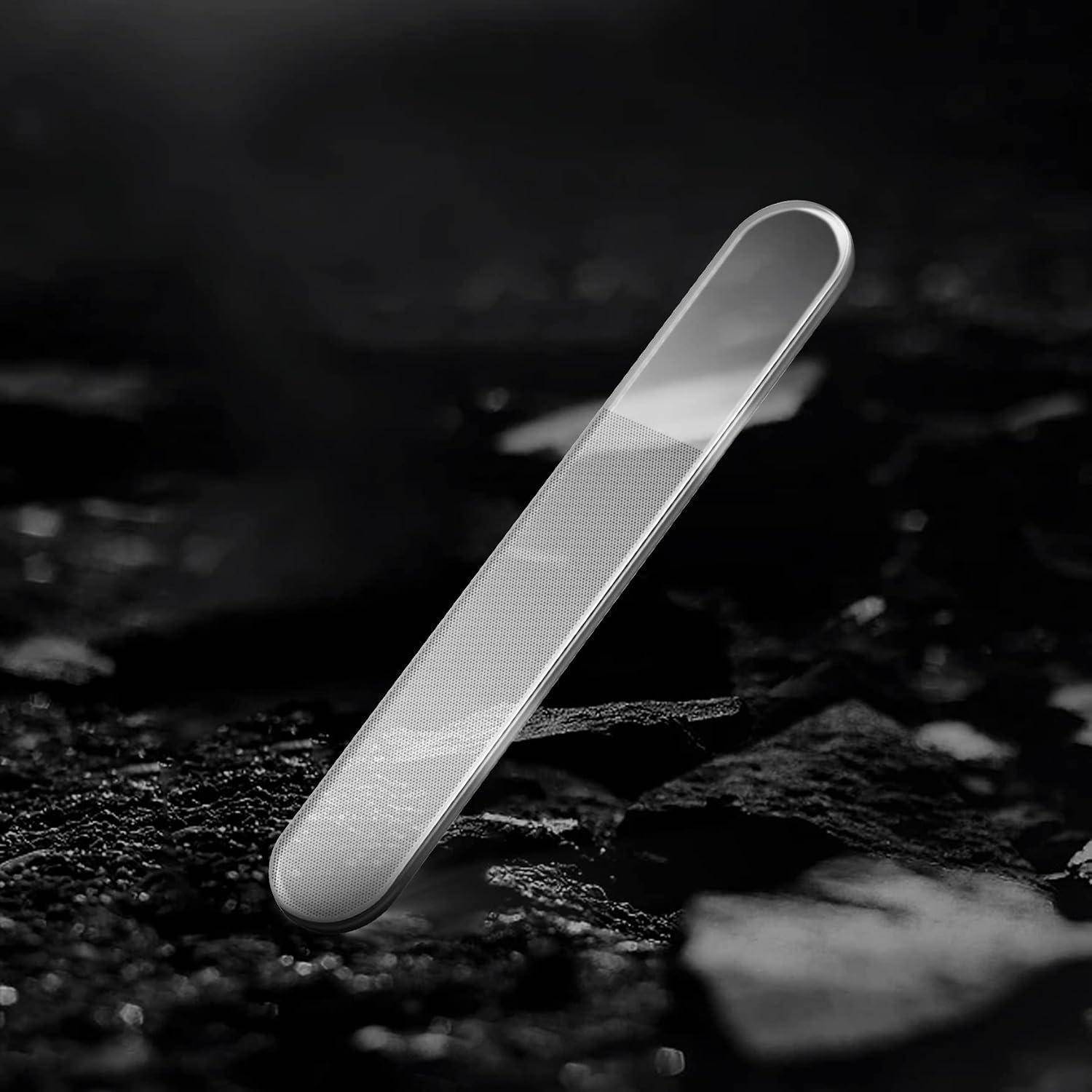 Silbernes Metall-Nagelfeile aufrecht auf einer dunklen strukturierten Oberfläche in schwarz-weißer Nahaufnahme.