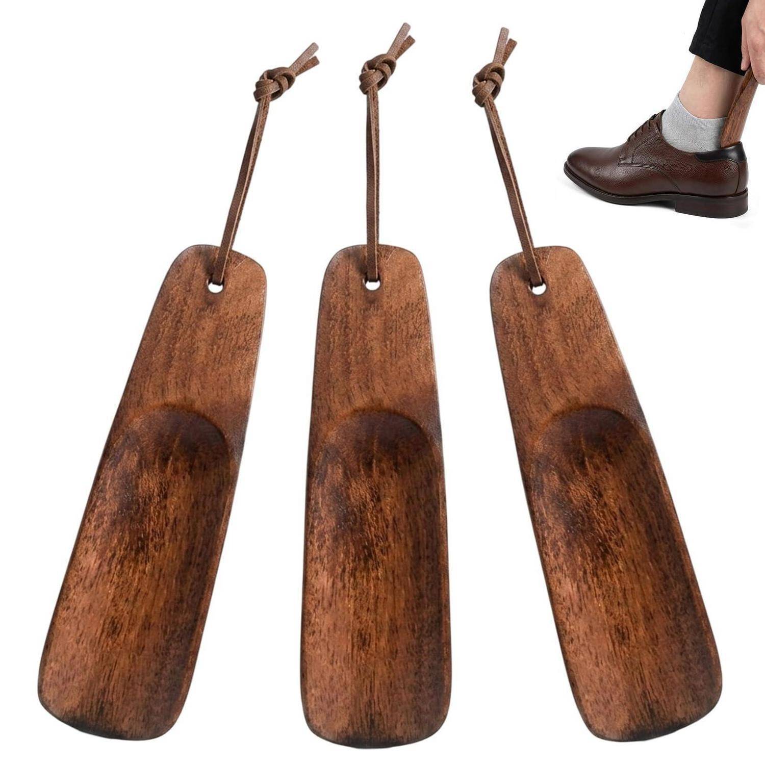 Drei Schuhlöffel aus Holz mit Aufhängeschleifen, neben einem Fuß mit Kleiderschuh zur Größenangabe dargestellt.