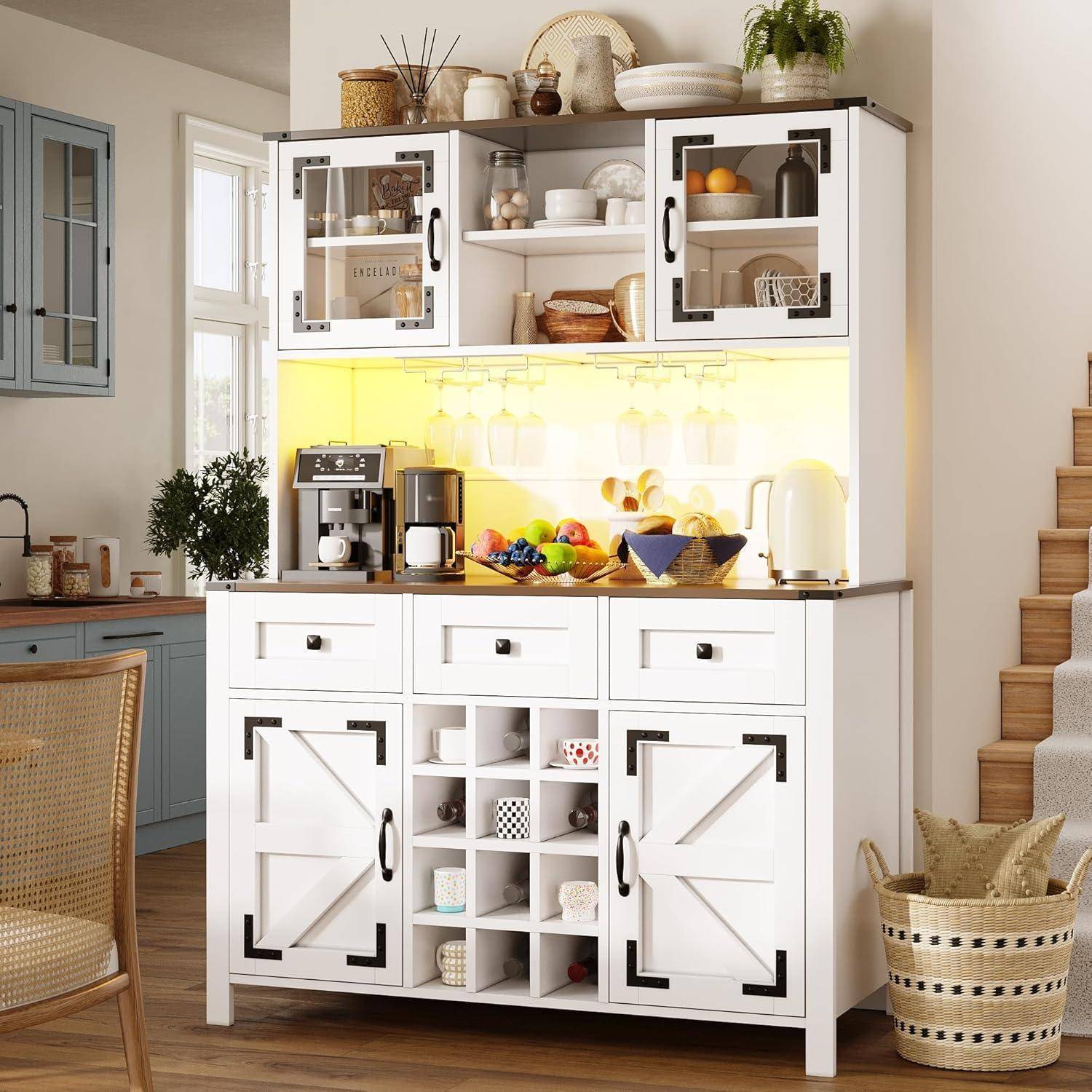 Helles Küchenbuffet mit weißen Schränken, Glastüren, offenen Regalen und beleuchteter Rückwand, auf dem eine Kaffeemaschine, Geschirr, Obst und geflochtene Körbe ausgestellt sind.