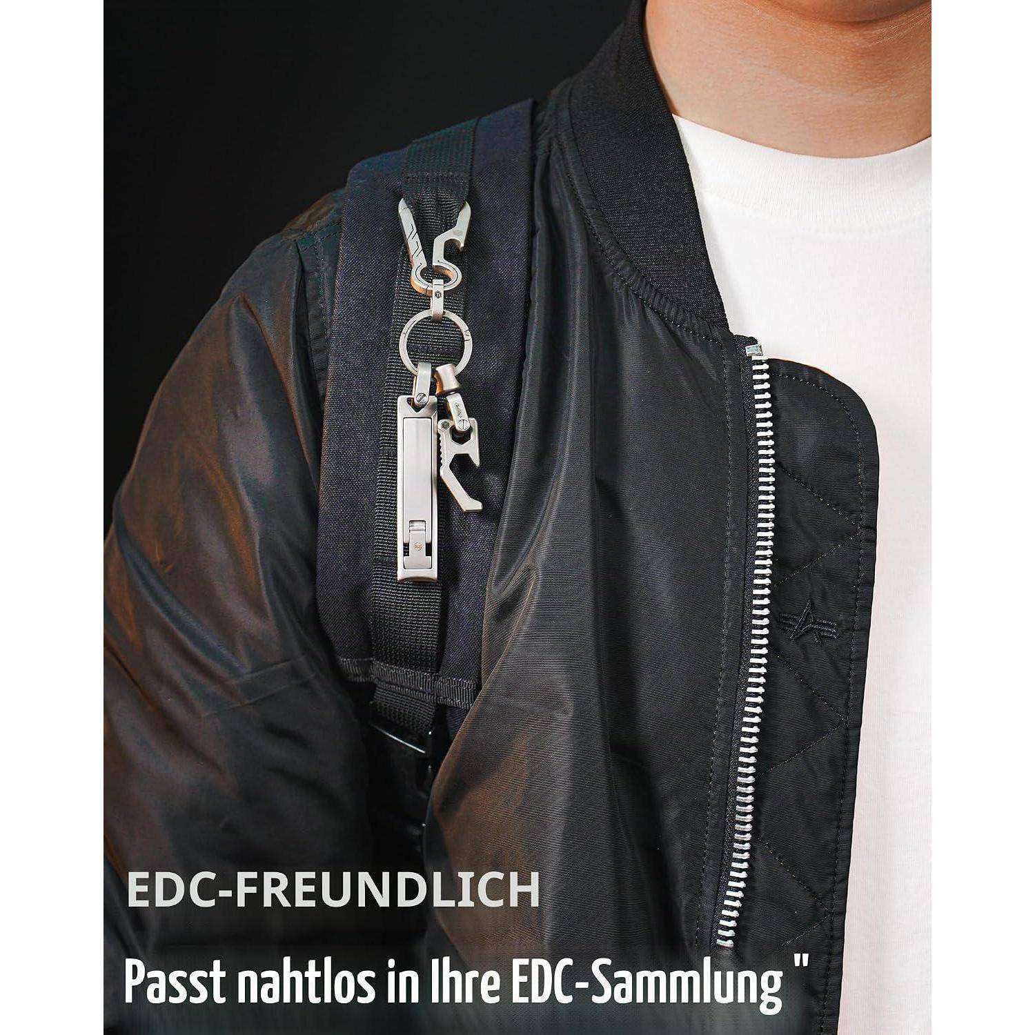 Nahaufnahme einer Person, die eine schwarze Jacke und einen Rucksack mit einem Metallschlüsselanhänger trägt, überlagert mit deutschem Text: 'EDC-FREUNDLICH Passt nahtlos in Ihre EDC-Sammlung