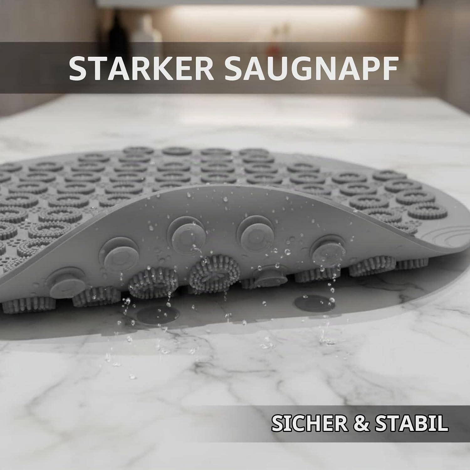 Graue Saugbadematte mit erhabenen Noppen und Saugnapfoberfläche, haftet auf einem nassen Marmorboden; Text lautet „STARKER SAUGNAPF