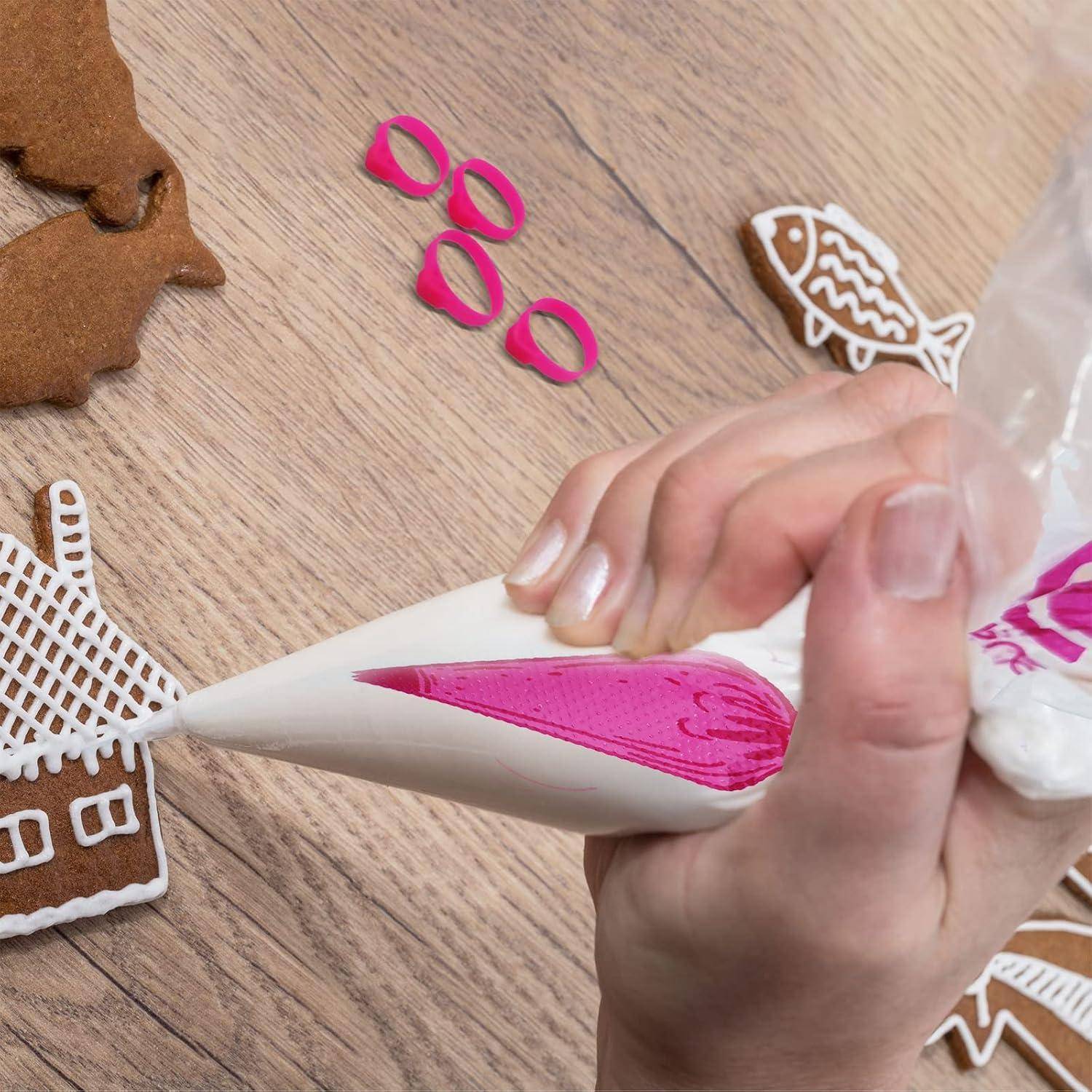 Hände, die rosafarbenes Zuckerguss aus einer Spritztüte auf ein Lebkuchenhäuschen auf einem Holztisch aufspritzen, mit anderen dekorierten Keksstücken in der Nähe.