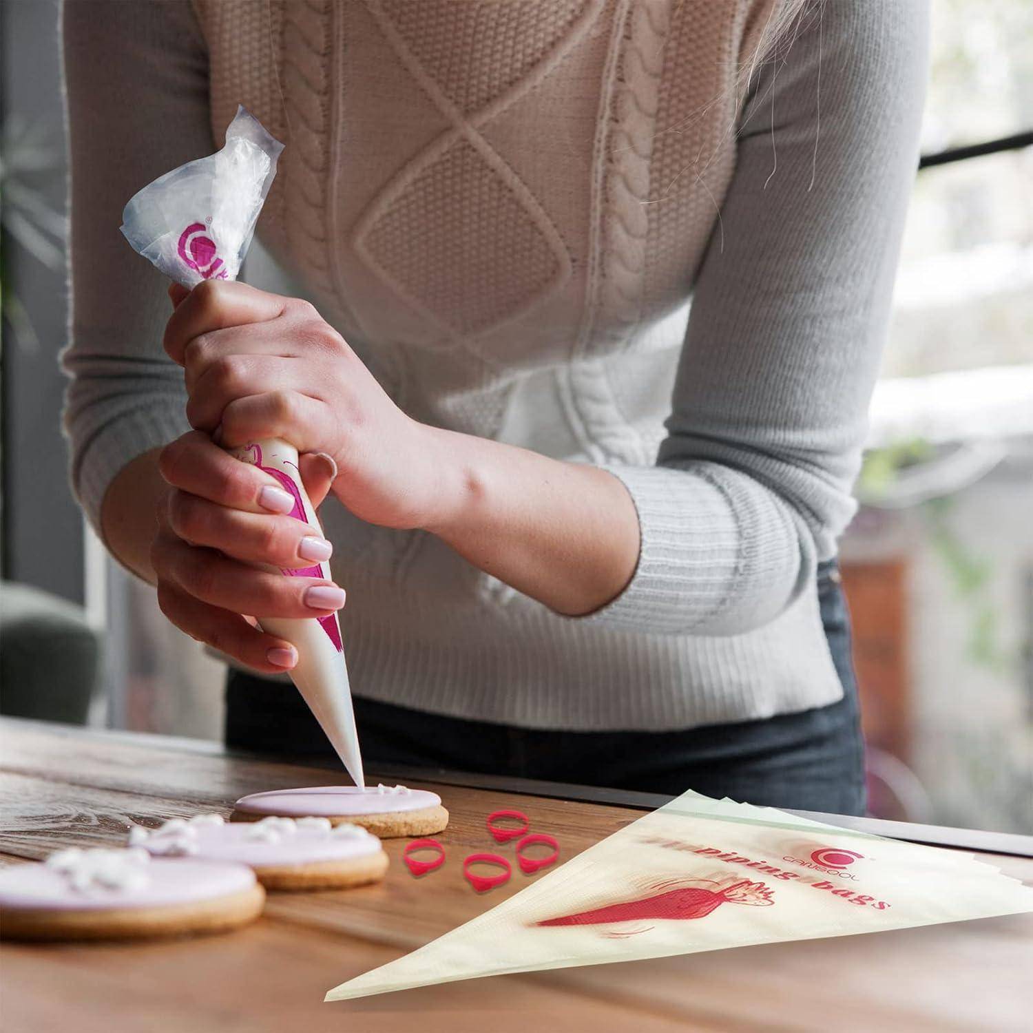 Eine Person trägt mit einer Spritztüte weiße Glasur auf runde Kekse auf einem Tisch auf, mit einer Spritztüte und Cookie-Dekorationswerkzeugen in der Nähe.
