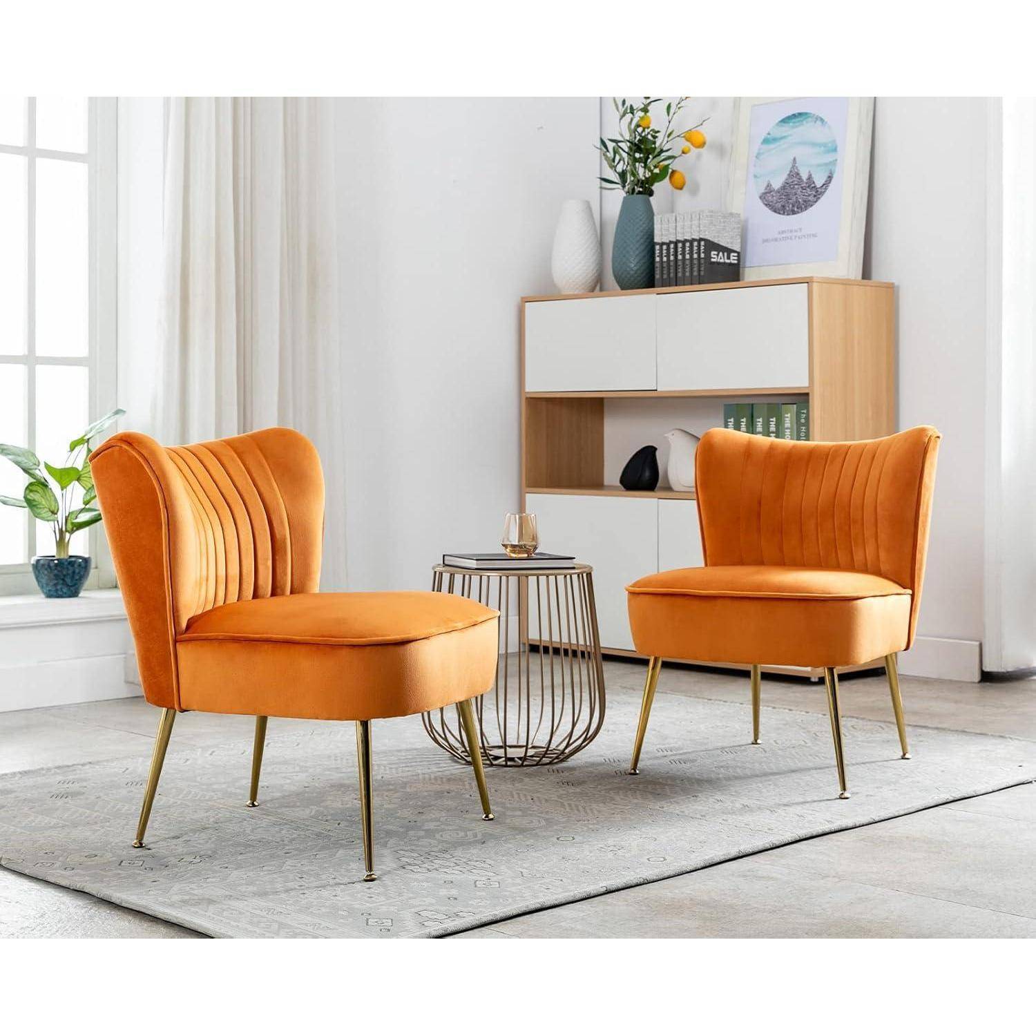 Zwei orange gepolsterte Akzentstühle mit goldenen Beinen in einem hellen Wohnzimmer, neben einem kleinen runden Beistelltisch und einem Schrank.