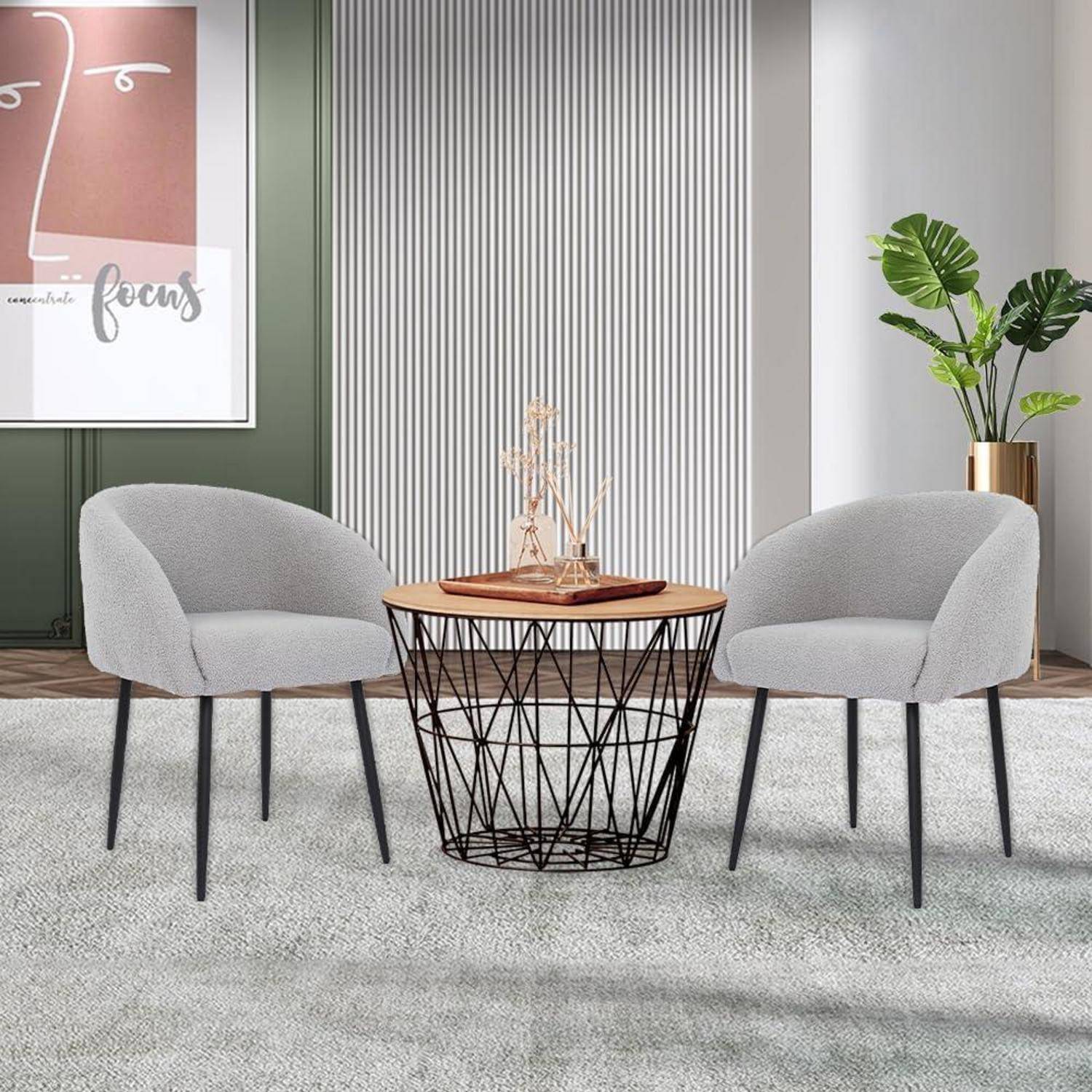 Moderner Sitzbereich mit zwei grau gepolsterten Stühlen, die einen runden Holz-Couchtisch mit Drahtgestell flankieren, in einem hellen Raum mit Wandkunst und einer Topfpflanze.