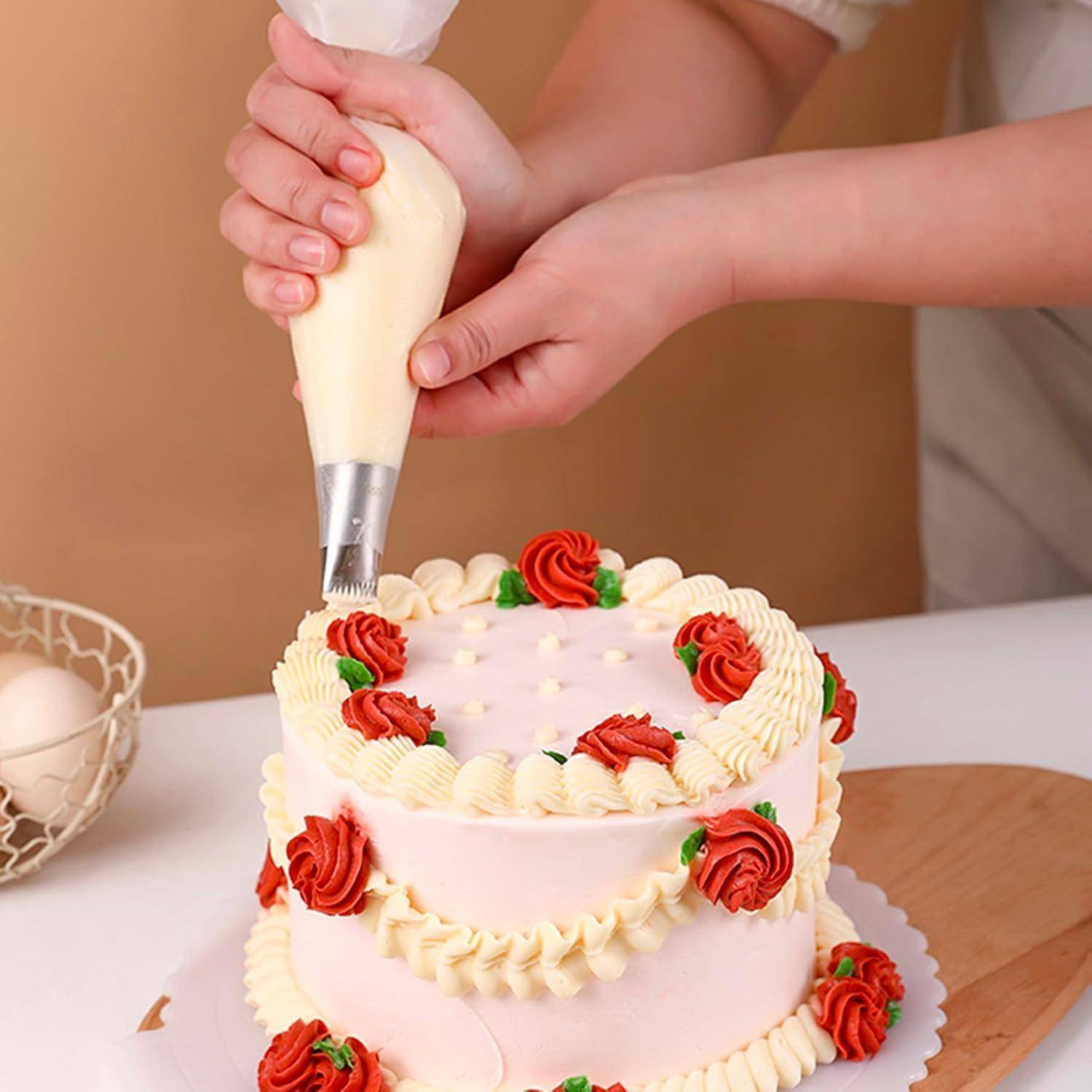 Hände, die weiße Glasur auf eine rosa Schichttorte mit roten und weißen Rosettendekorationen spritzt.
