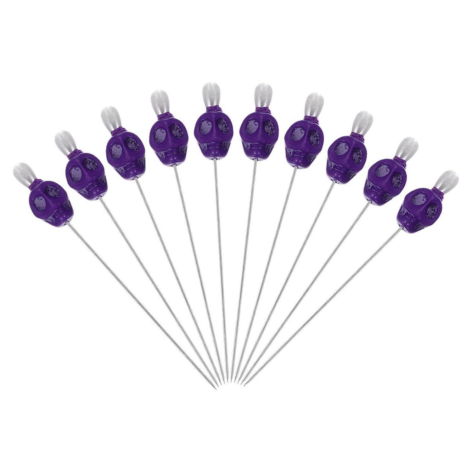 Satz violetter Cocktailspieße mit Totenkopfaufsätzen, fächerförmig angeordnet, mit silbernen Stielen und weißen Quastenaufsätzen auf einfachem weißem Hintergrund.