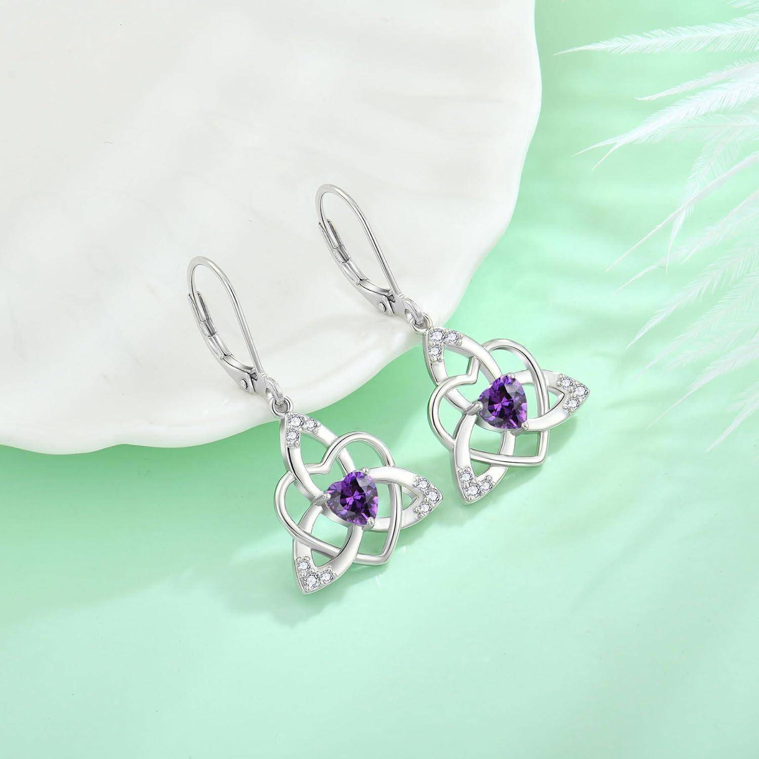 Paar silberner Tropfen-Ohrringe mit violetten Edelsteinen und herzförmigen Designs auf hellmintgrünem Hintergrund.