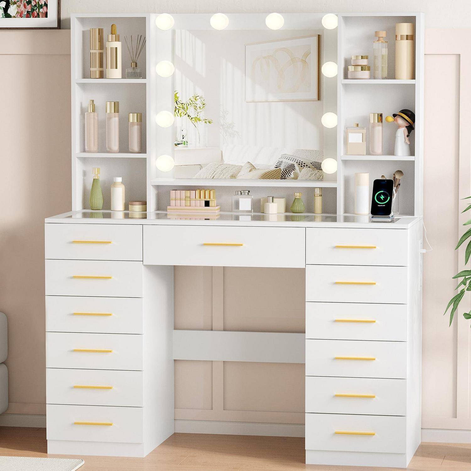 Weißer Frisiertisch mit Spiegel und Leuchten, flankiert von Regalen und Schubladen, die Kosmetikprodukte und Dekoration in einem hellen Schlafzimmer enthalten.