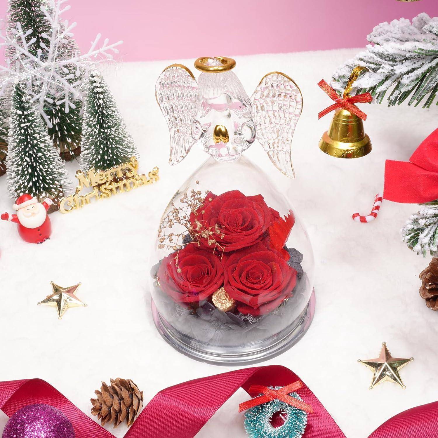 Glaskuppel mit roten Rosen im Inneren und Engelsflügeln oben drauf, arrangiert als weihnachtliches Blumengeschenk inmitten festlicher Weihnachtsdekoration.