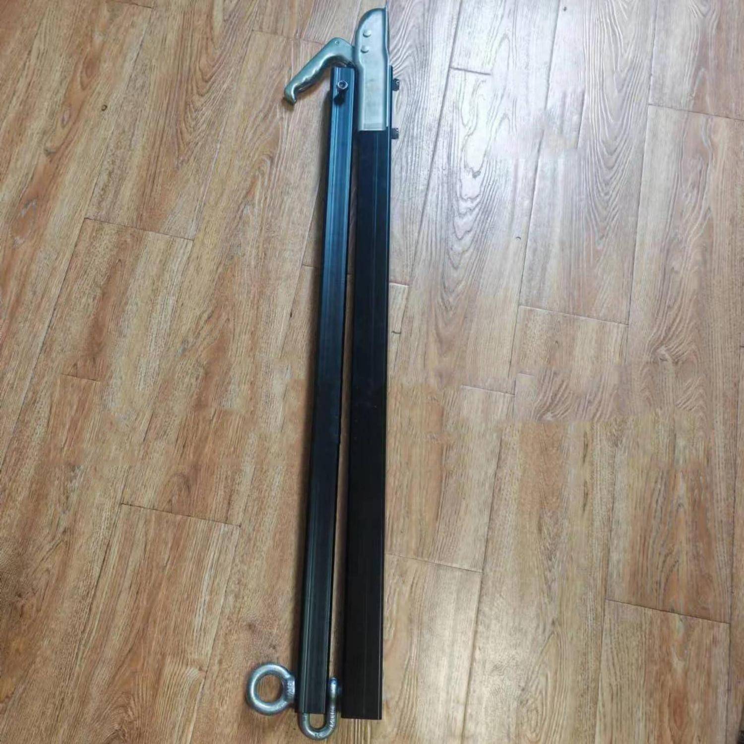 Metallisches Faltgestell oder Stützbein auf einem Holzboden, mit einem Haken an der Oberseite und einem Kreisring am unteren Ende.