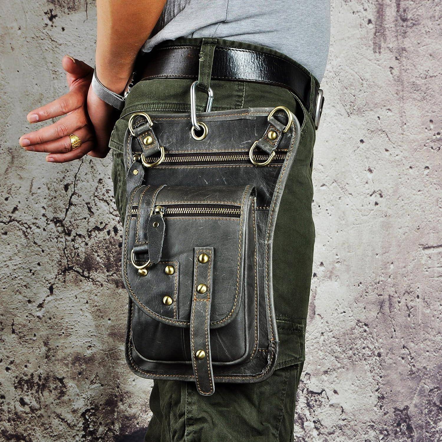 Eine Person trägt eine übergroße schwarze Leder-Utilitytasche, die an einem grünen Hosenriemen vor einer strukturierten Wand befestigt ist.