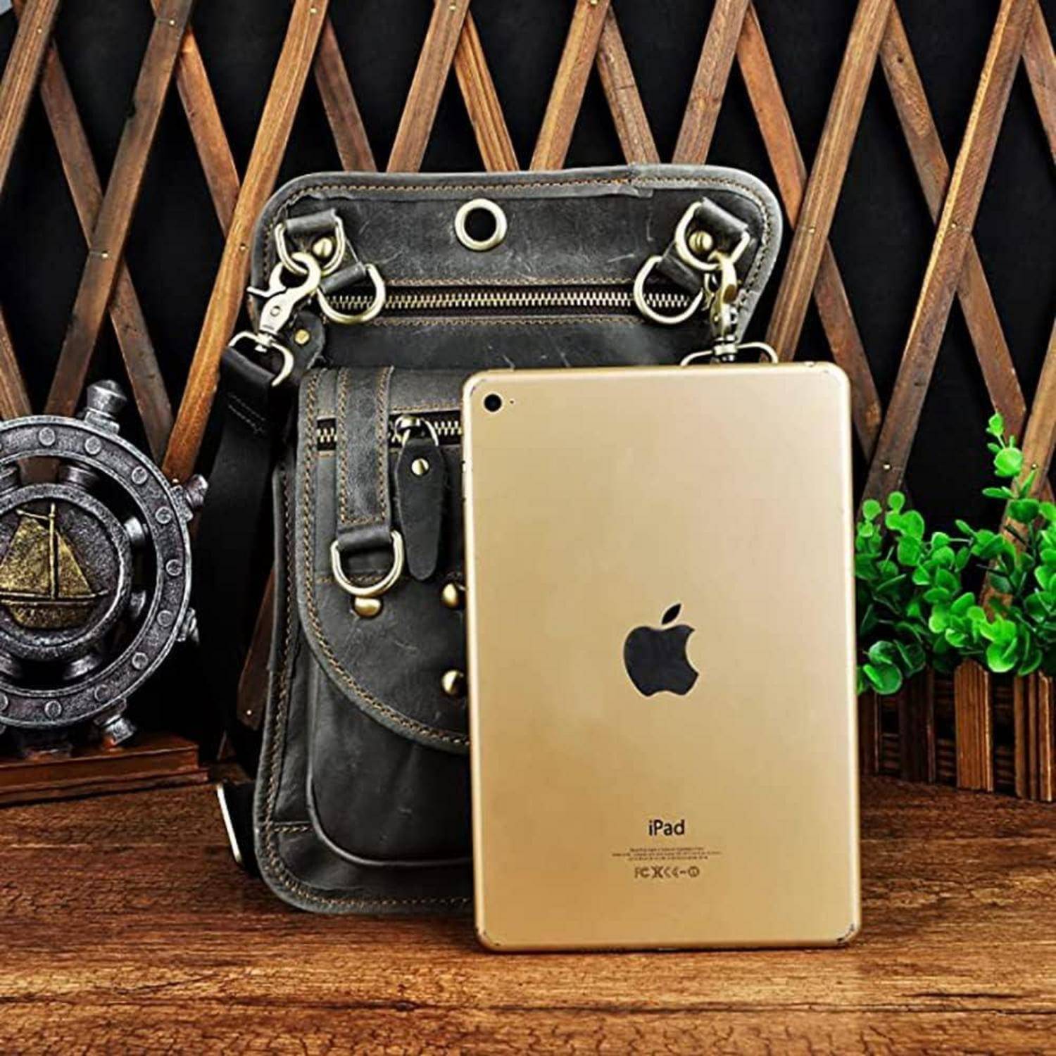 Ein goldenes iPad, das an einer schwarzen Ledertasche auf einer Holzoberfläche lehnt, mit dekorativen Nautik- und Pflanzenelementen im Hintergrund.
