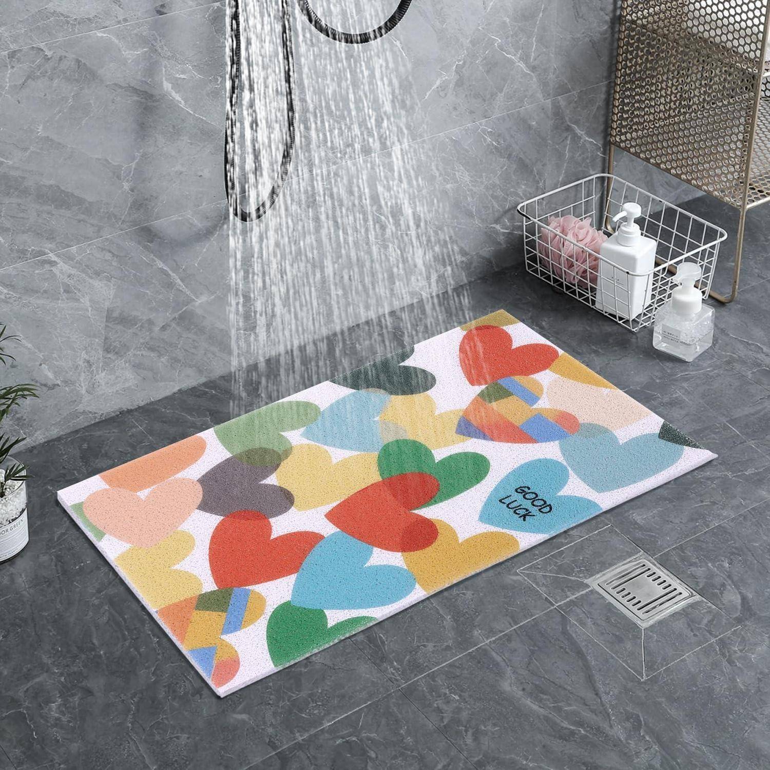 Bunte Badematte mit Herzenmuster unter fließendem Duschwasser in einem gefliesten Badezimmer, mit Abfluss und Toilettenkorb in der Nähe.