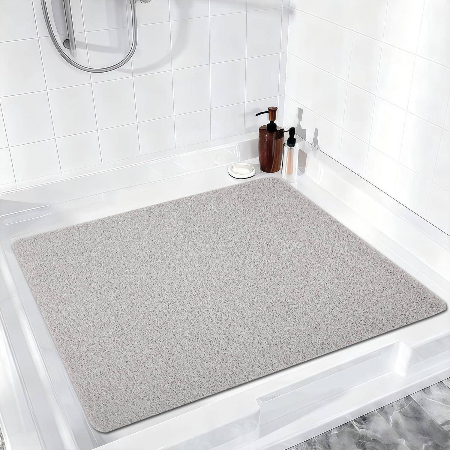 Grauer rutschfester Badezimmerteppich auf einem weißen Duschboden mit Seifenspendern in der Ecke.