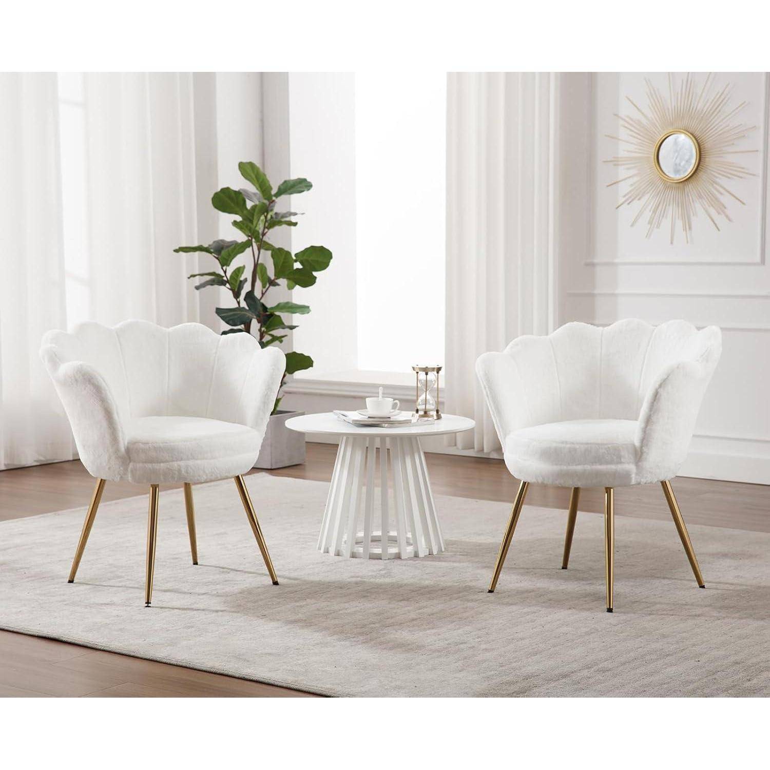 Zwei weiße gepolsterte Akzentstuhlstühle mit goldfarbenen Beinen stehen sich an einem kleinen runden weißen Tisch in einem hellen, minimalistischen Wohnzimmer mit einer Pflanze und Wandkunst gegenüber.
