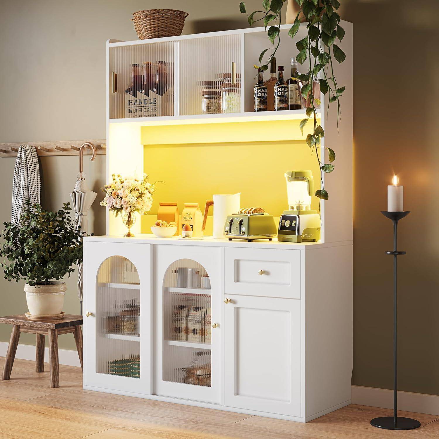 Weiße Küchenanrichte mit leuchtendem gelbem Gegenlicht, Regale mit Gläsern und Tellern, Toaster, Blumen und hängende Rankenpflanze in einem gemütlichen Zimmer.
