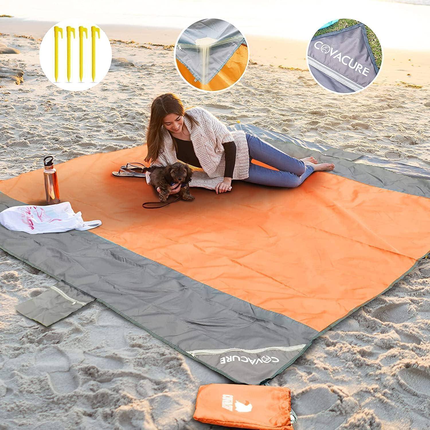 Frau, die sich mit einem kleinen Hund auf einer großen orangefarbenen Stranddecke ausstreckt, mit einer Wasserflasche und einem Tragekoffer in der Nähe im Sand.