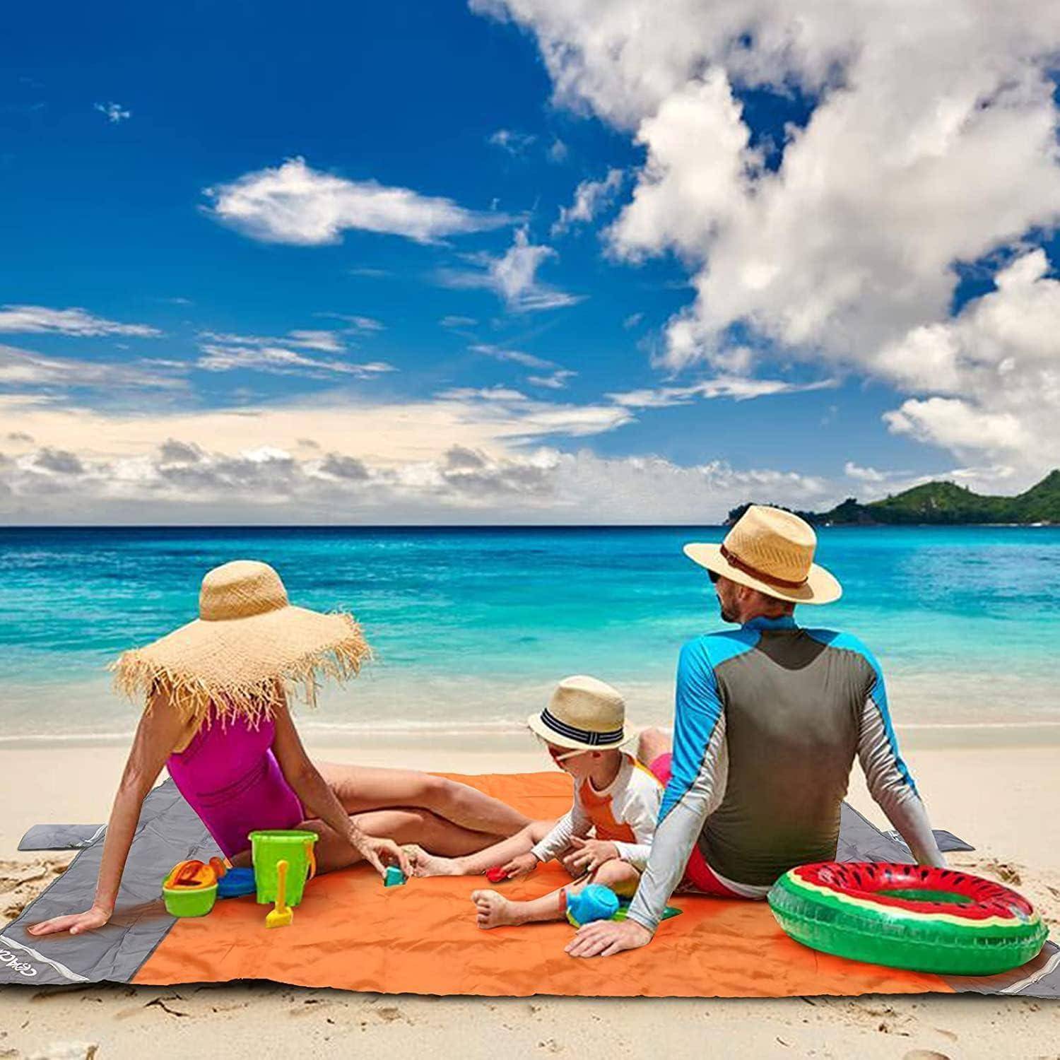 Familie aus drei Personen entspannt sich an einem tropischen Strand, sitzt auf Handtüchern am türkisfarbenen Wasser, mit Sandspielzeugen und einem Wassermelonen-Schwimmer.